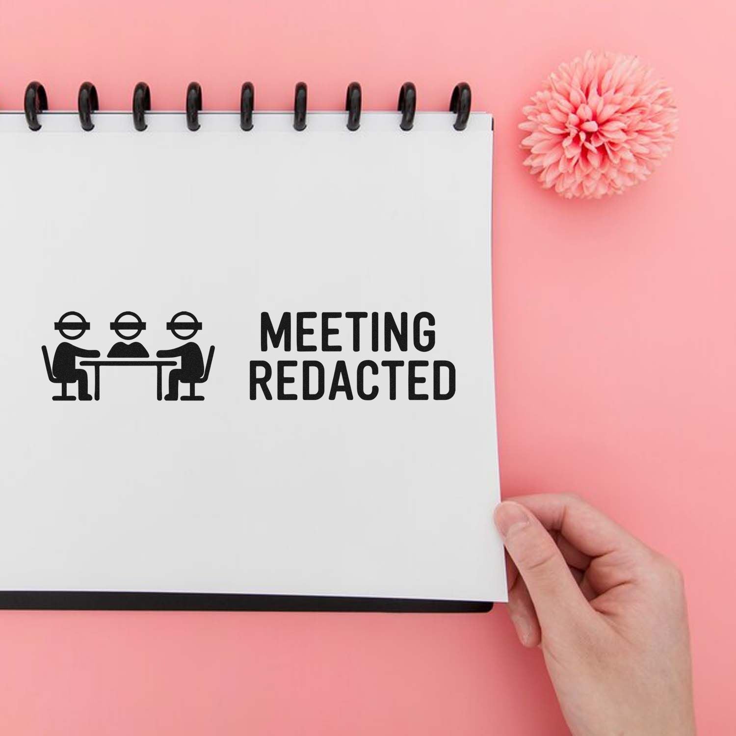 Meeting redacted rubber stamp on notebook for office records, with meeting icon and pink desk background.