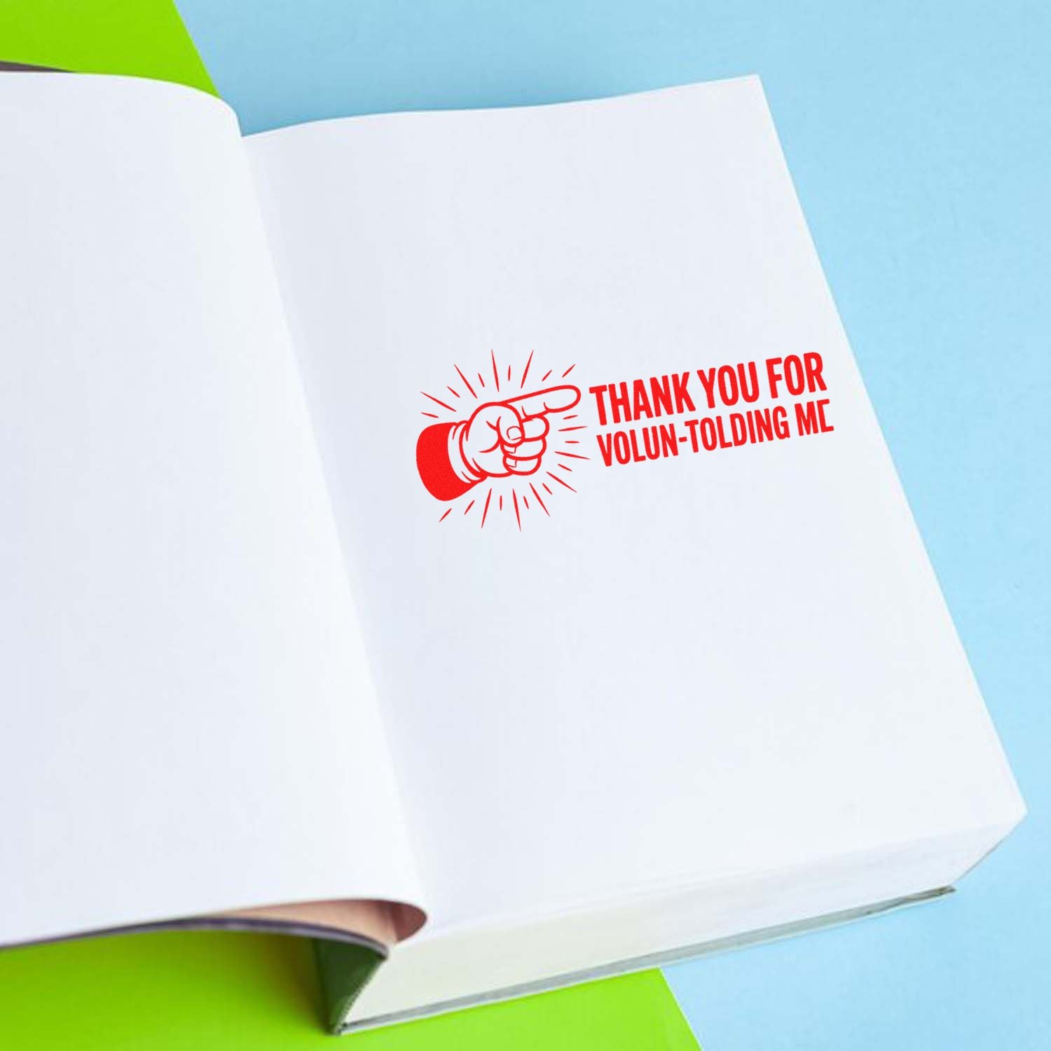 Funny red rubber stamp on open book reads Thank You for Volun-tolding Me, ideal for teacher and volunteer appreciation.