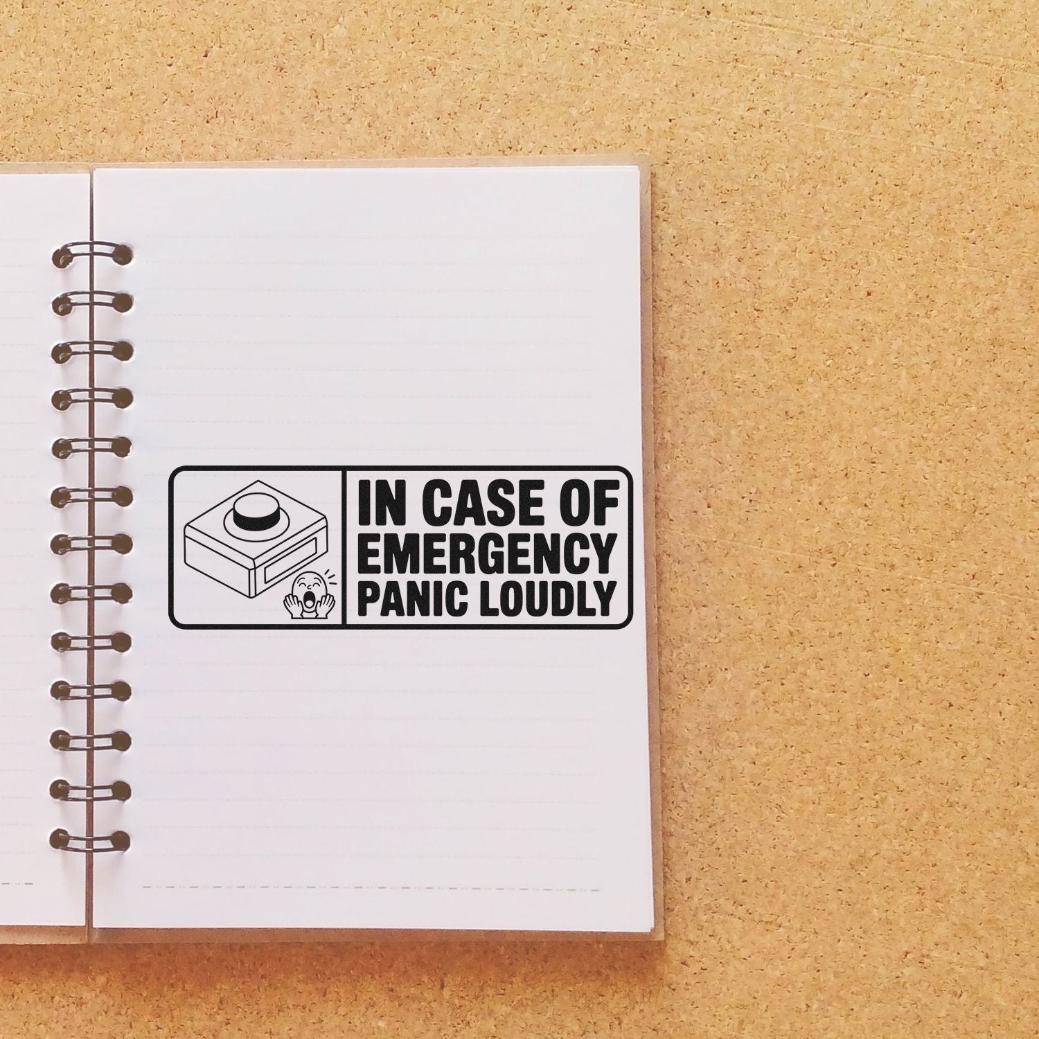 Rubber stamp reading In Case of Emergency, Panic Loudly on notebook page, featuring an emergency button icon.