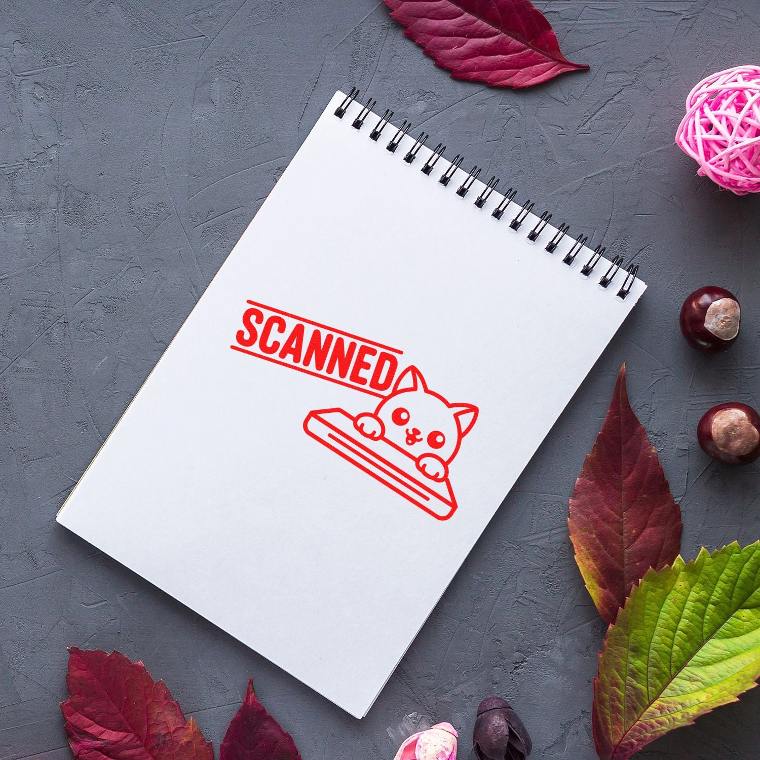 Red SCANNED cat rubber stamp impression on a spiral notebook, ideal for marking documents or handmade stationery.
