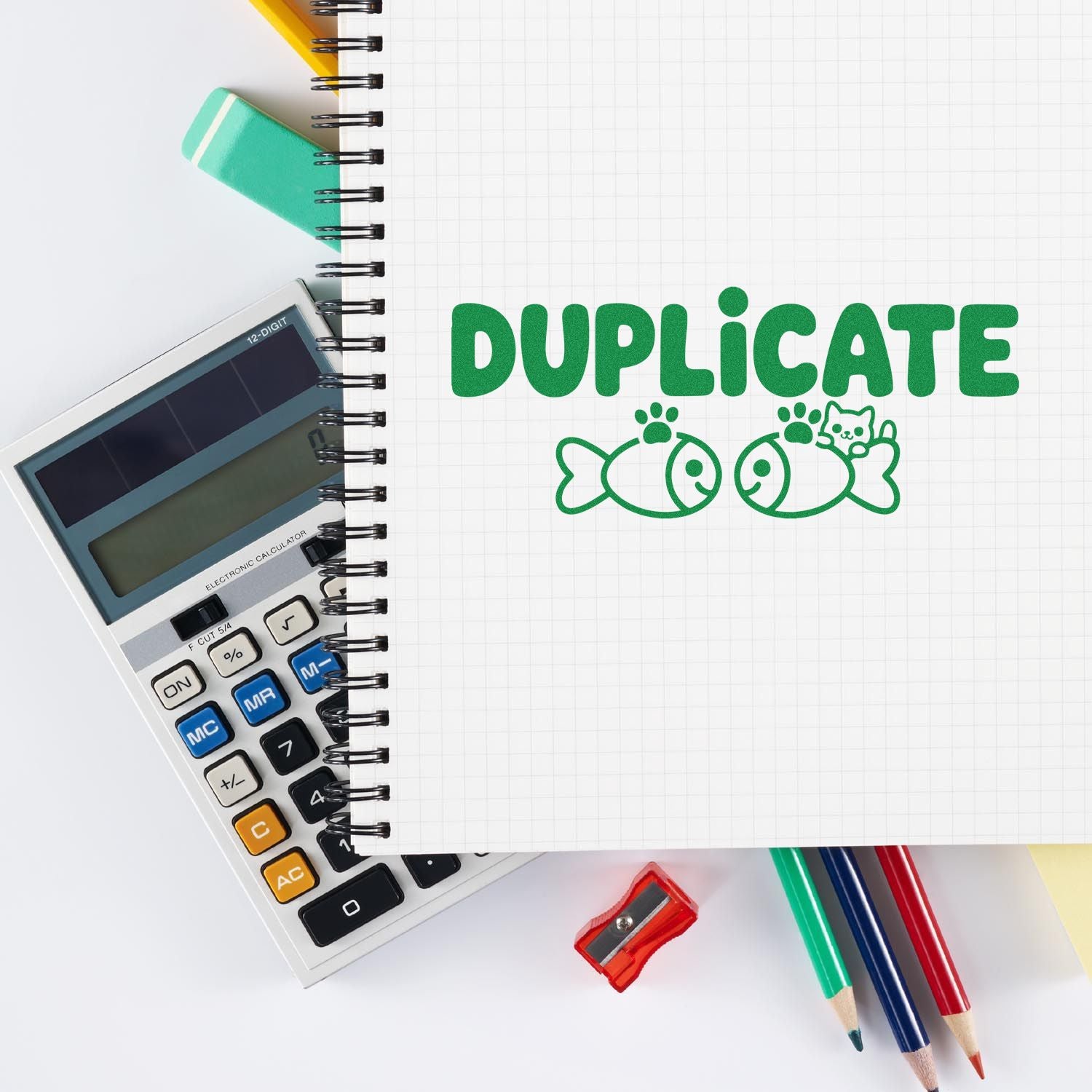 Green duplicate rubber stamp on notebook beside calculator, pencils and sharpener for office paperwork and document copying.