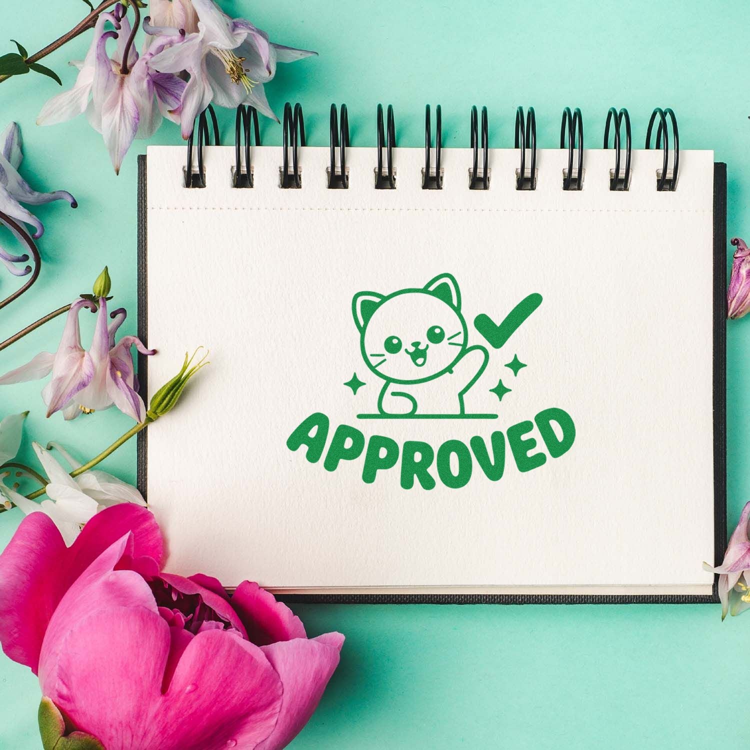 Cute approved cat rubber stamp design on a notebook, displayed with flowers on a mint green background.