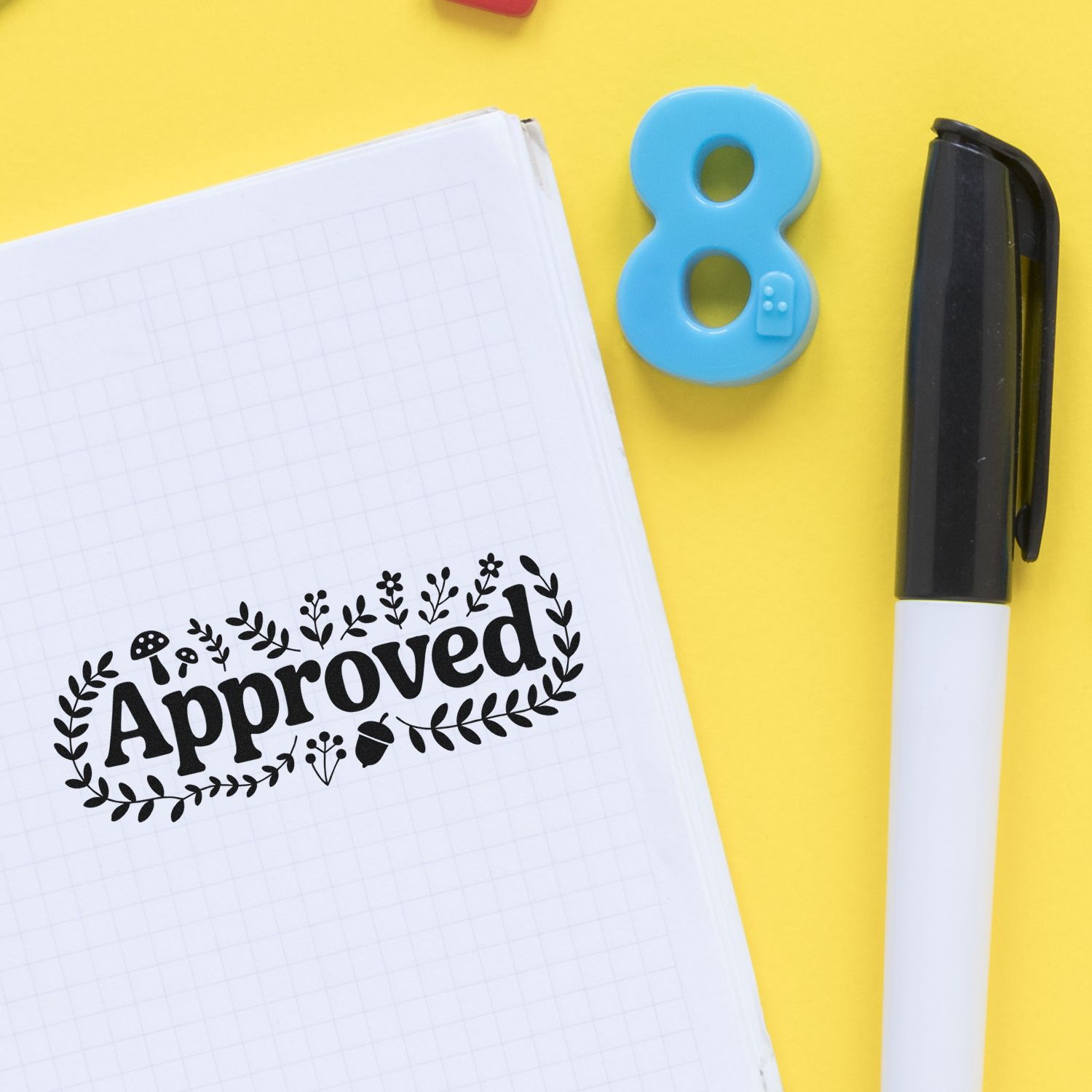 Approved rubber stamp impression on notebook beside pen, ideal for office approval and stationery organization.