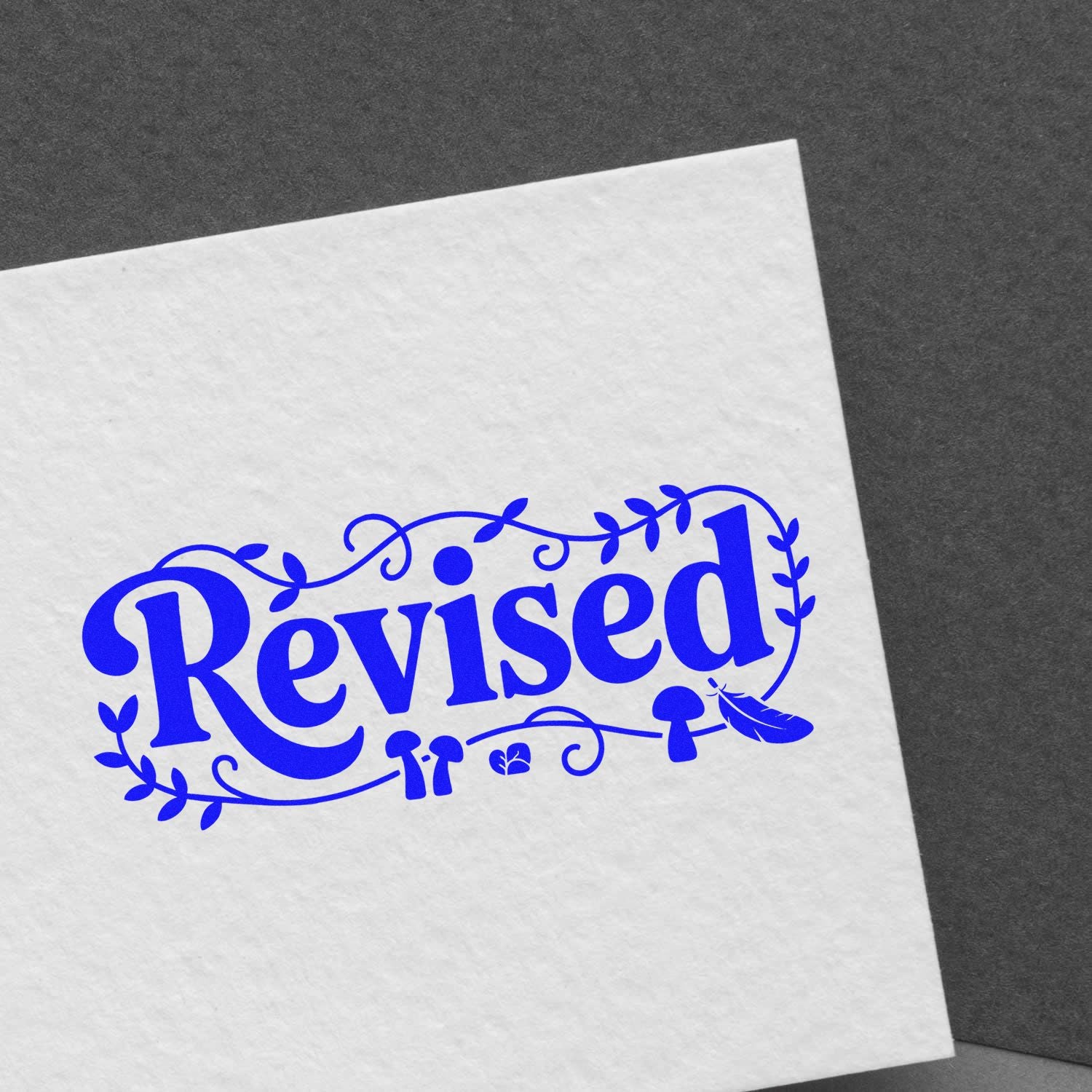 Blue Revised rubber stamp impression with decorative leaves on white paper for document approval.