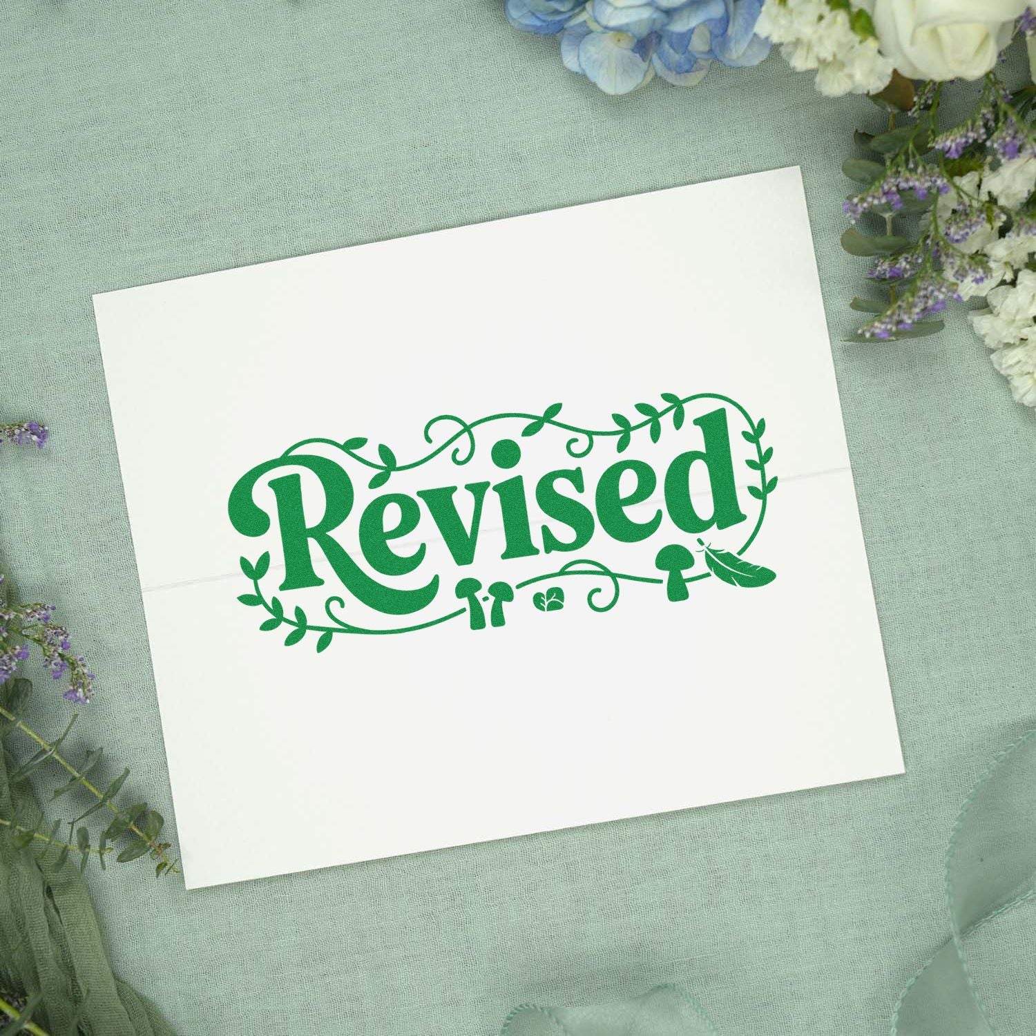 Green Revised rubber stamp with floral vine design on white paper, ideal for office, planner, or craft use.