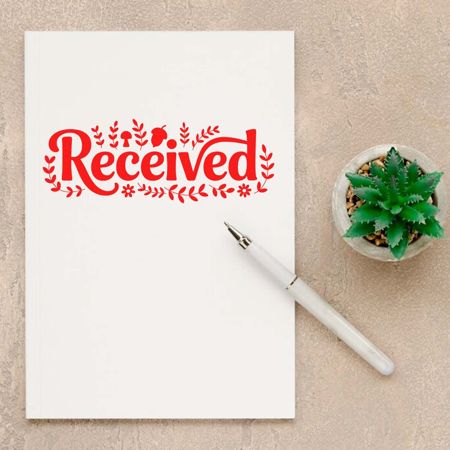 Red Received rubber stamp impression on white paper with pen and plant, ideal for office mail processing and crafting.