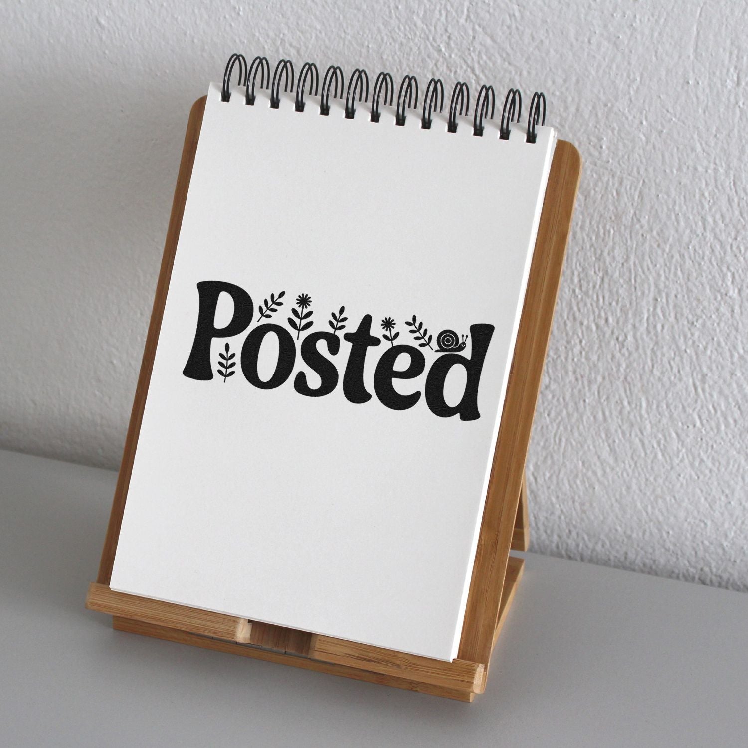 Posted rubber stamp design preview on a spiral notepad, featuring floral accents and a wooden display stand.