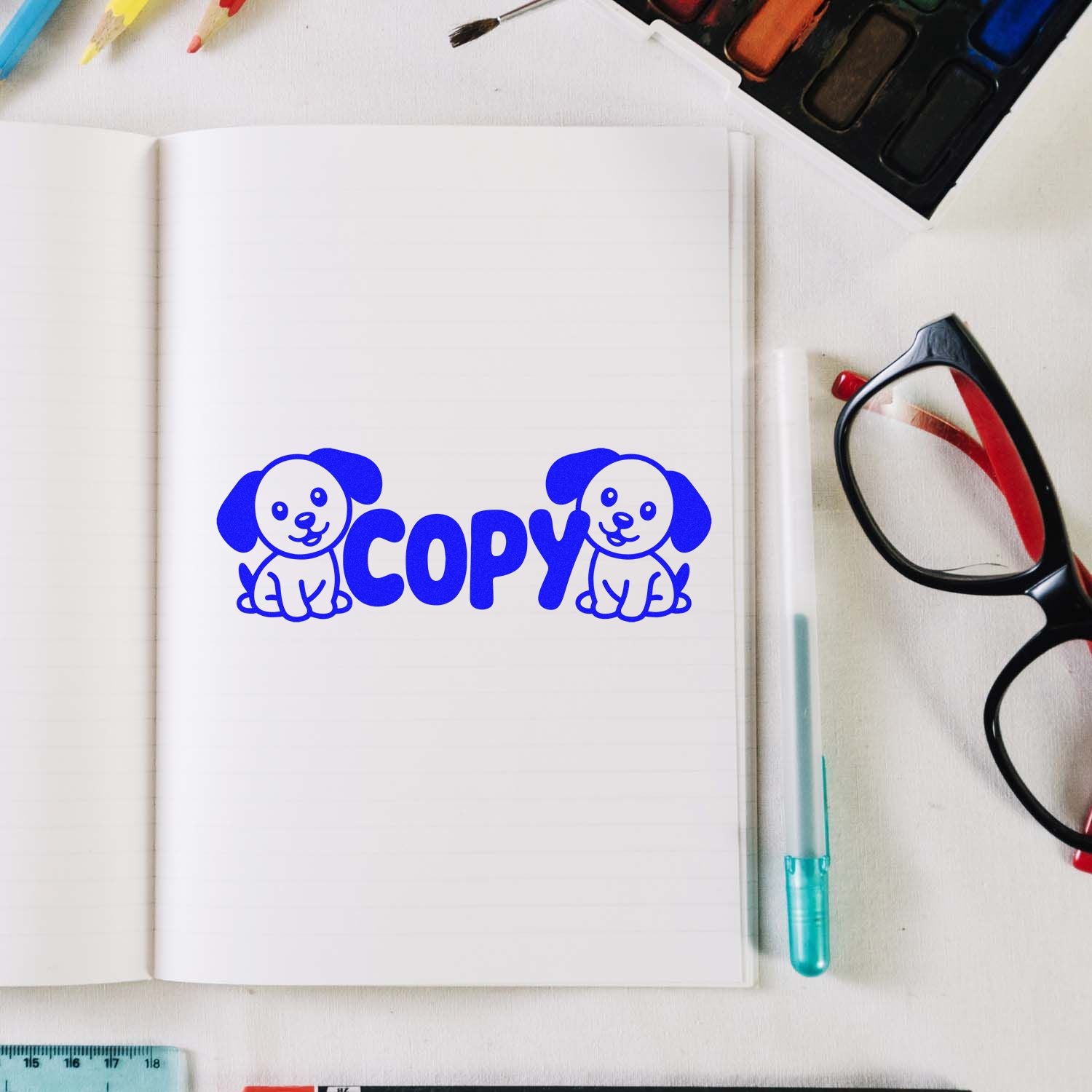 Blue COPY rubber stamp design with dog icons on notebook, surrounded by stationery and art supplies for custom rubber stamps.