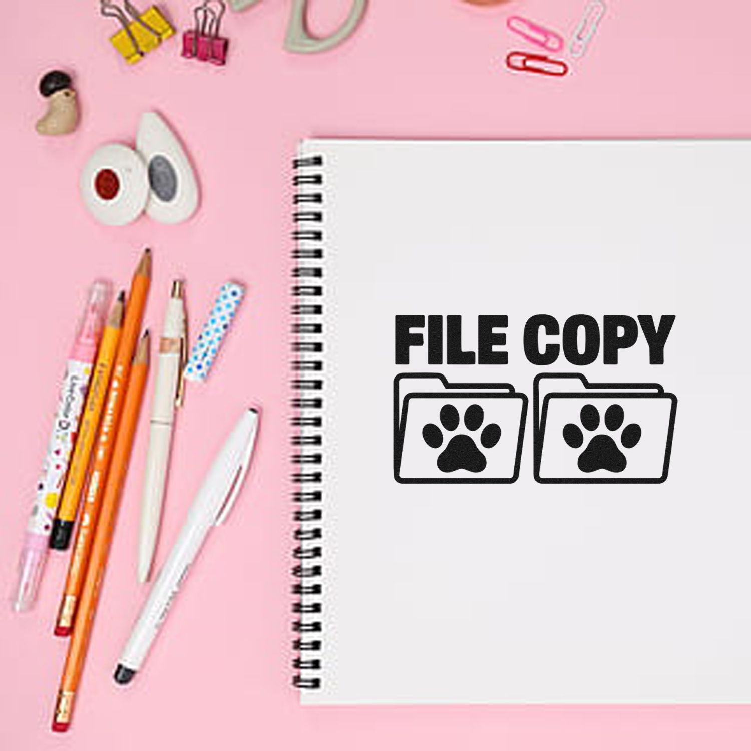 File Copy rubber stamp design on spiral notebook with paw print folders, styled flat lay with pens on pink background.