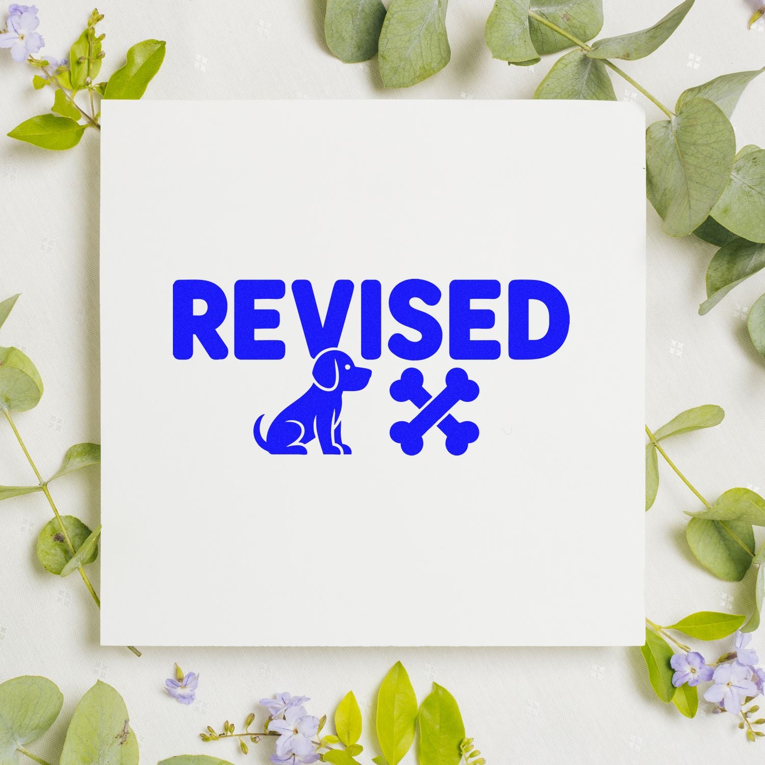 Blue REVISED rubber stamp with dog and bones icon on white paper, ideal for document review and approvals.