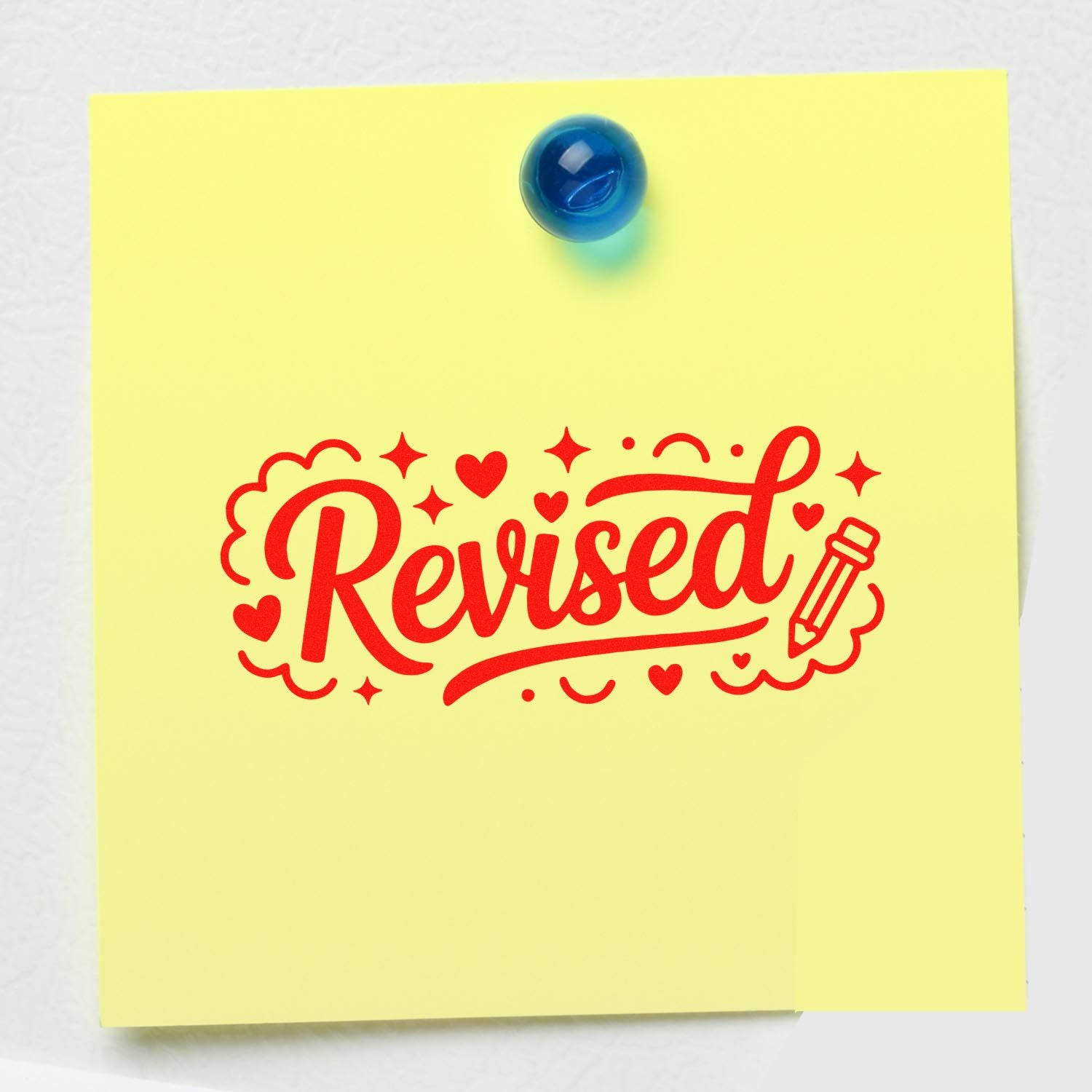 Red revised rubber stamp with hearts and pencil on yellow sticky note, marking a document update or approval.