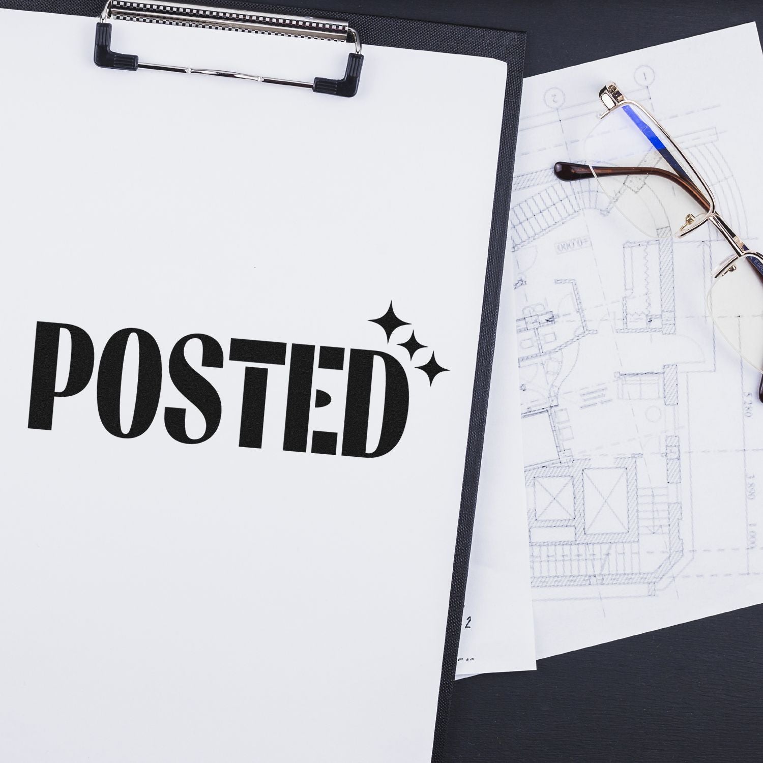 Posted rubber stamp on clipboard beside architectural plans and eyeglasses for document approval workflow.