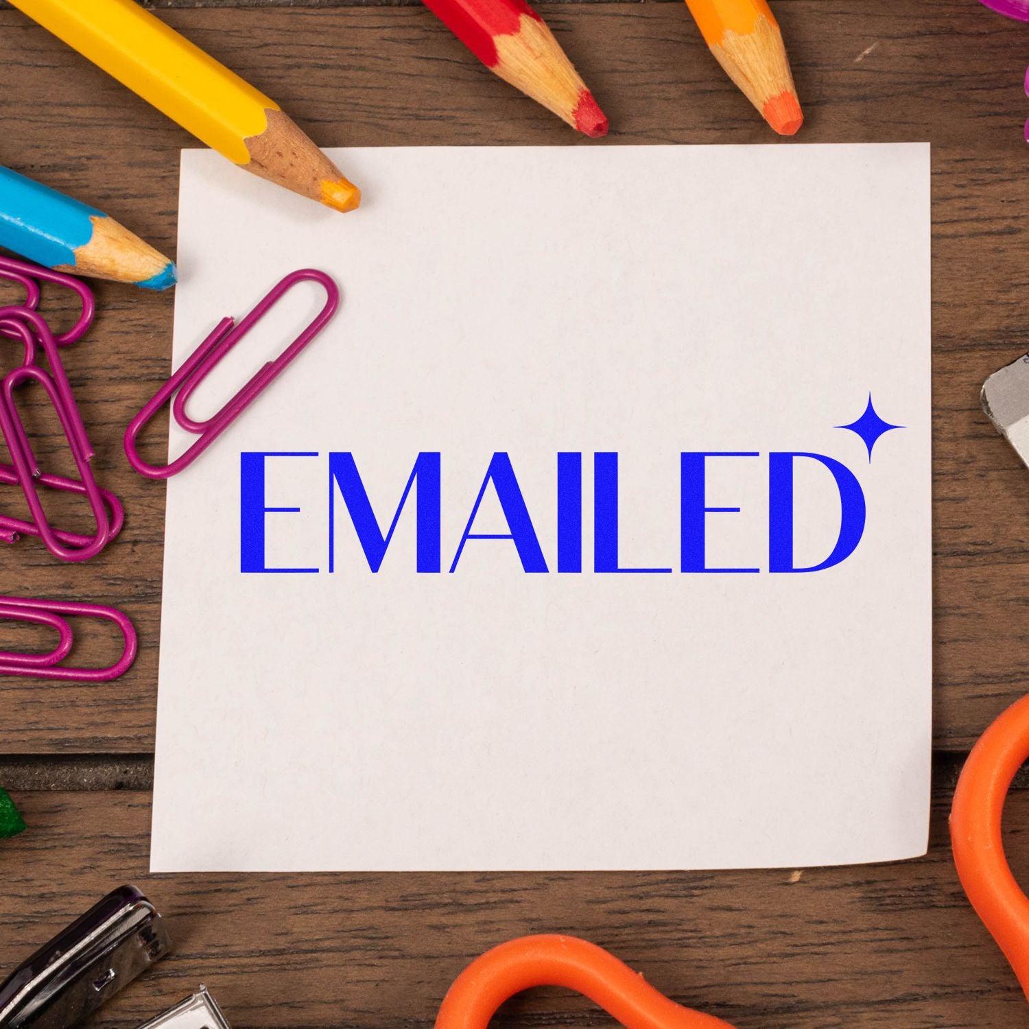 Blue Emailed rubber stamp impression on white paper with pencils and paper clips, ideal for office mail tracking.