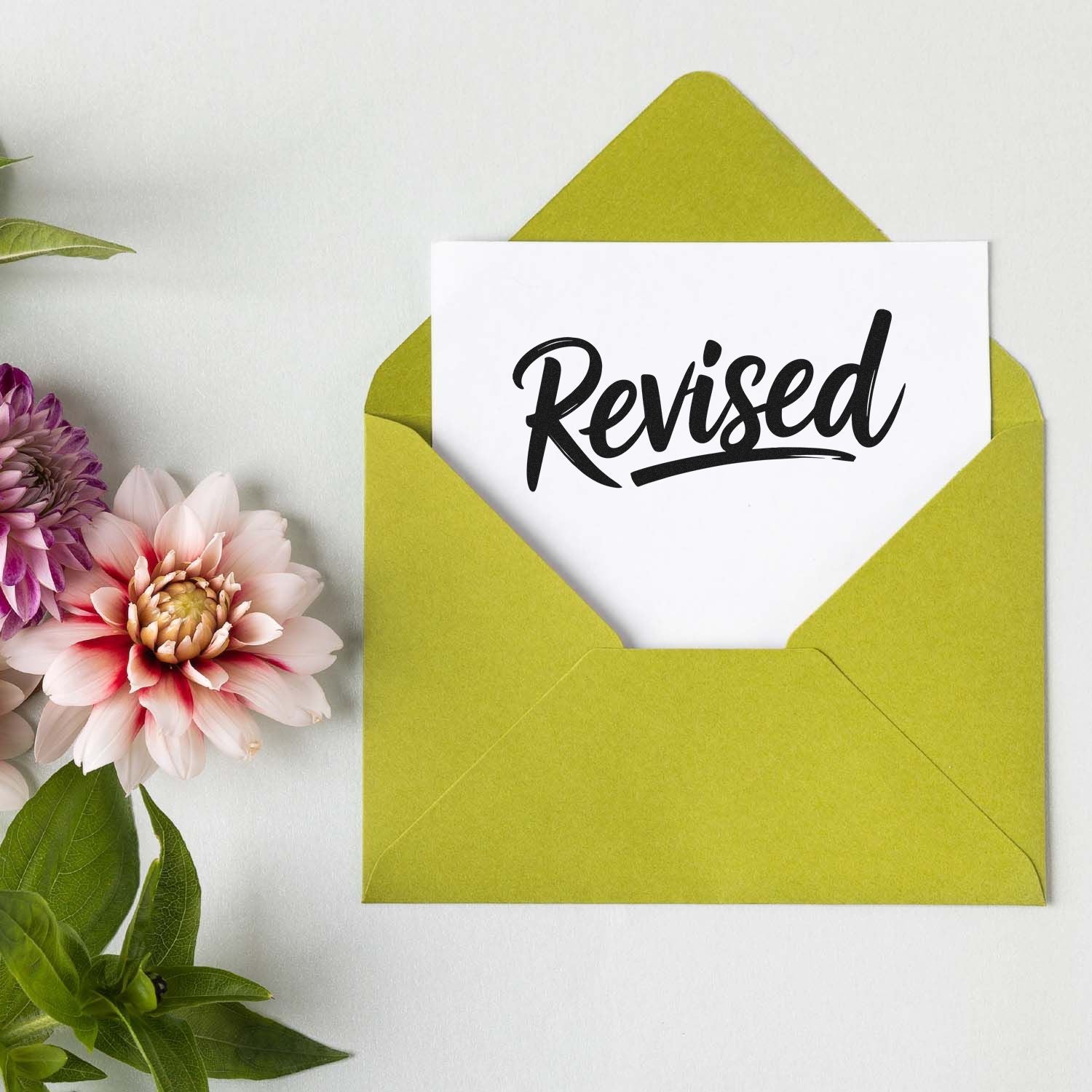 Revised rubber stamp imprint on a white card in a lime green envelope, ideal for office document review and approval.