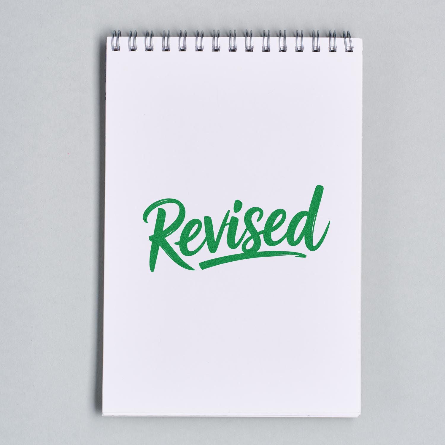 Green Revised rubber stamp on a blank notepad page for office document review and approval marking.