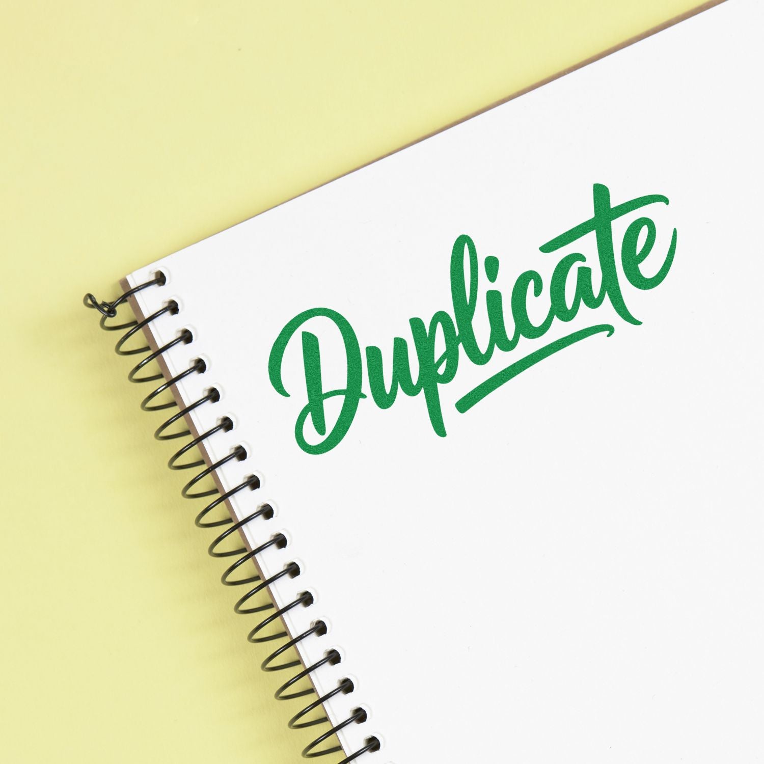 Green Duplicate rubber stamp on a white spiral notebook, ideal for office document labeling and copy control.