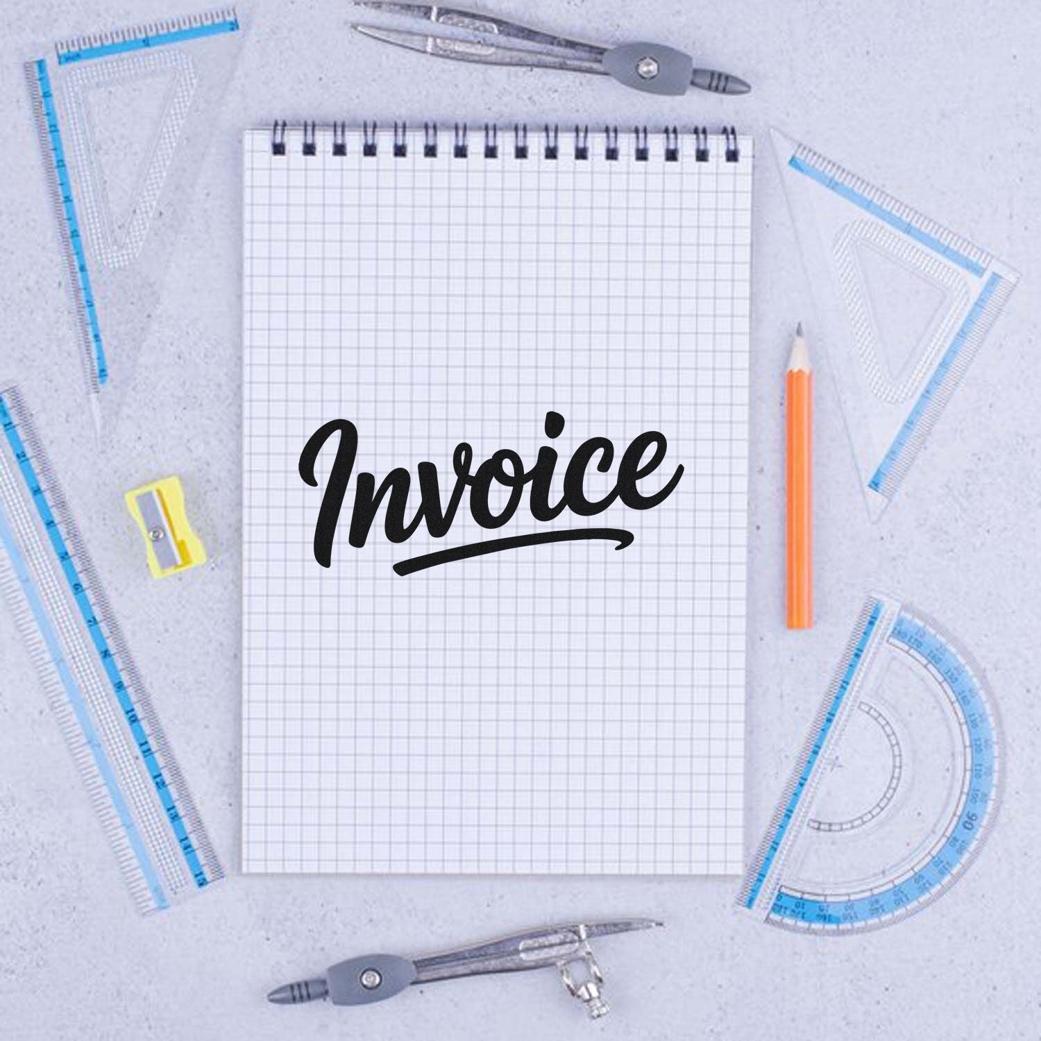 Invoice rubber stamp design on a graph notebook, surrounded by drafting tools for office, accounting, and bookkeeping use.
