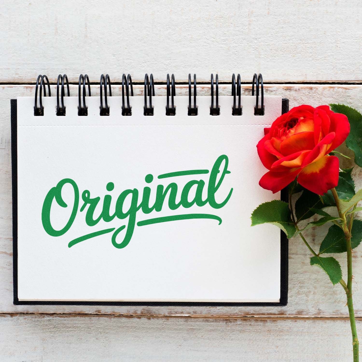 Original rubber stamp mockup in green script on a notebook beside a red rose.