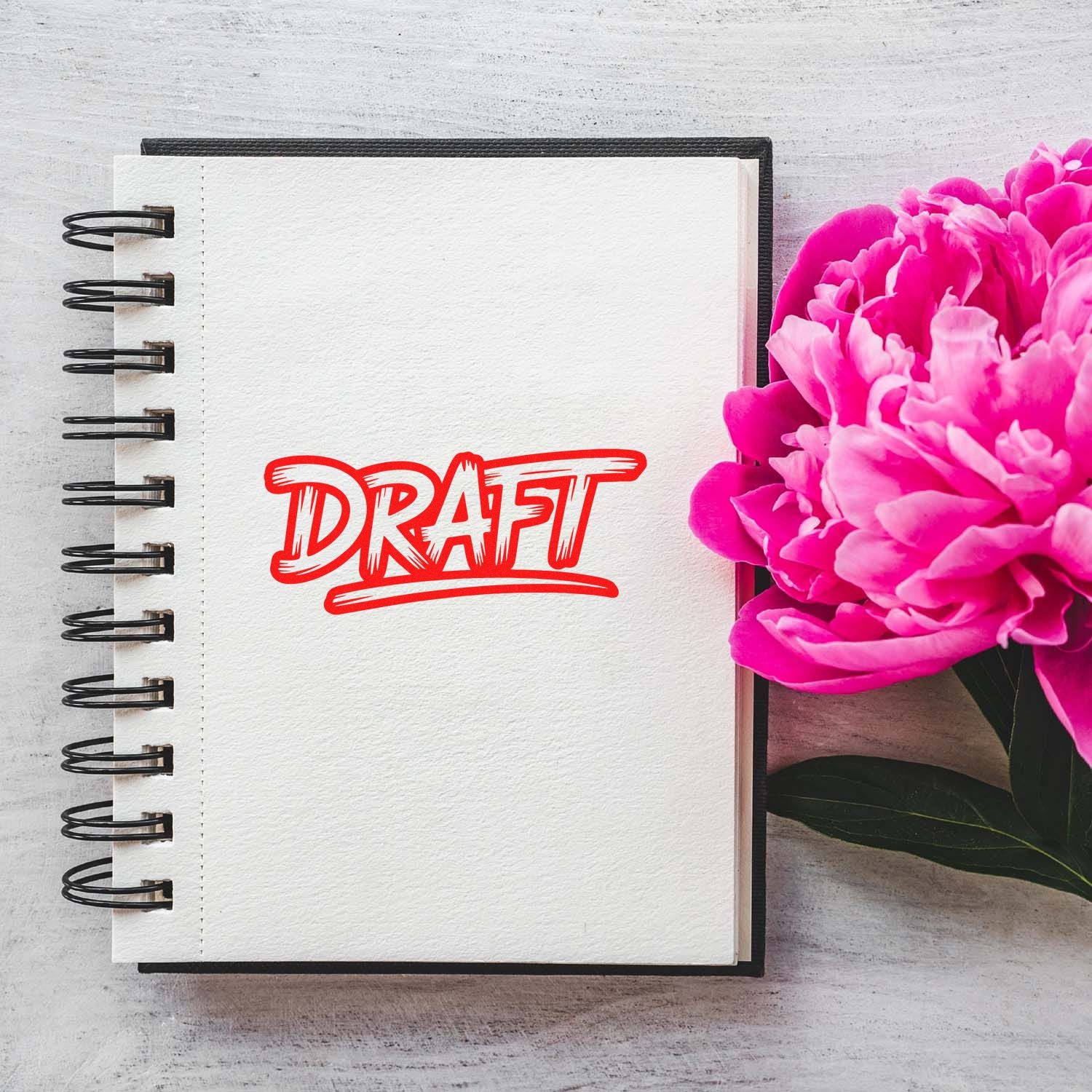 Red DRAFT rubber stamp impression on notebook page with pink flowers, ideal for stationery and office proofing.