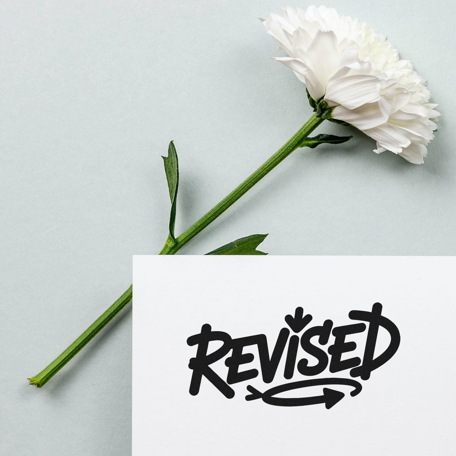 Revised rubber stamp on paper beside white flower, ideal for document approval and office workflow.