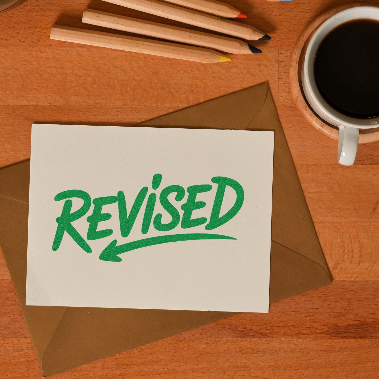 Revised rubber stamp on a card with envelope, pencils and coffee, marking edited documents on a desk.