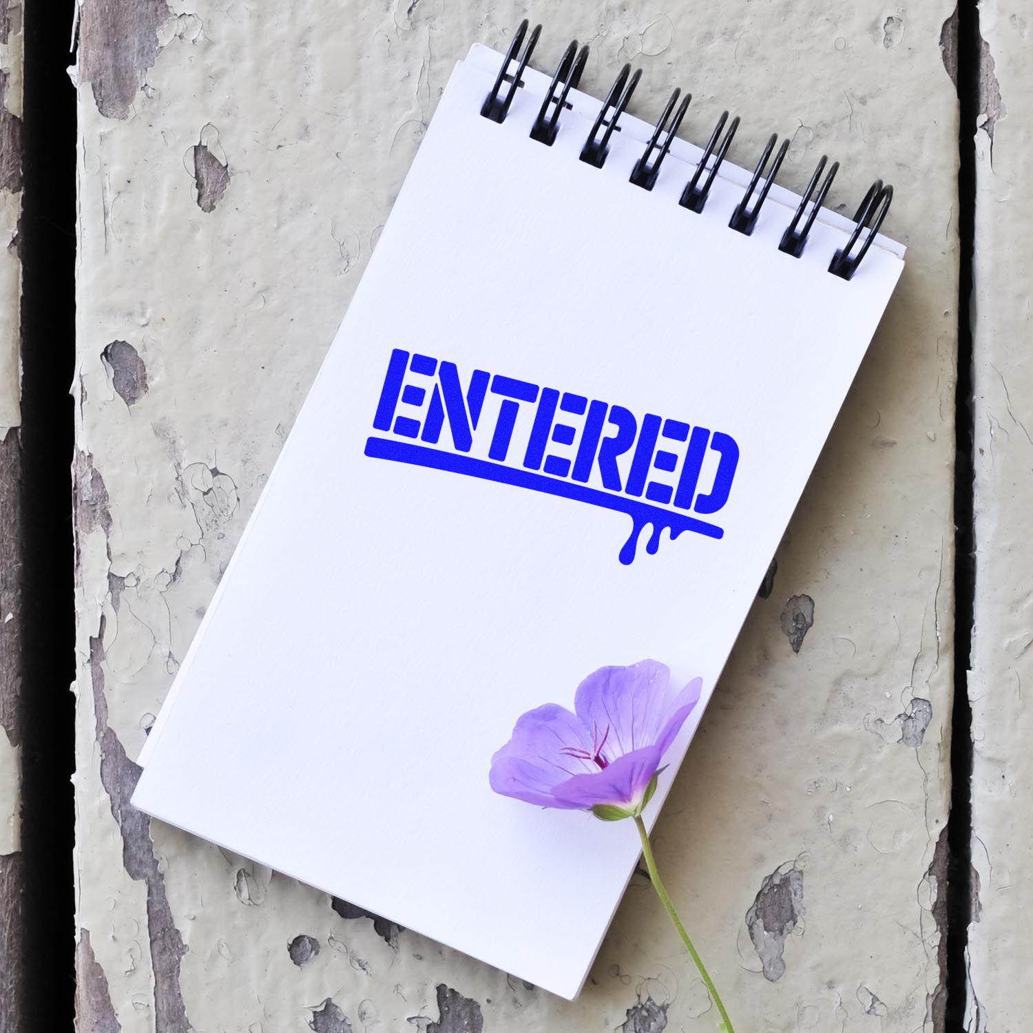 Blue ENTERED rubber stamp on a spiral notepad, ideal for office document status marking, records, and filing.