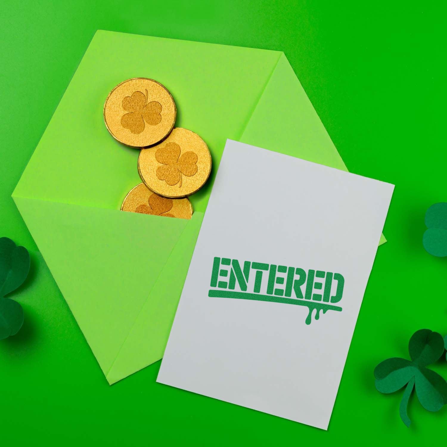 Green ENTERED rubber stamp imprint on card beside a St. Patricks Day envelope and shamrock coins.