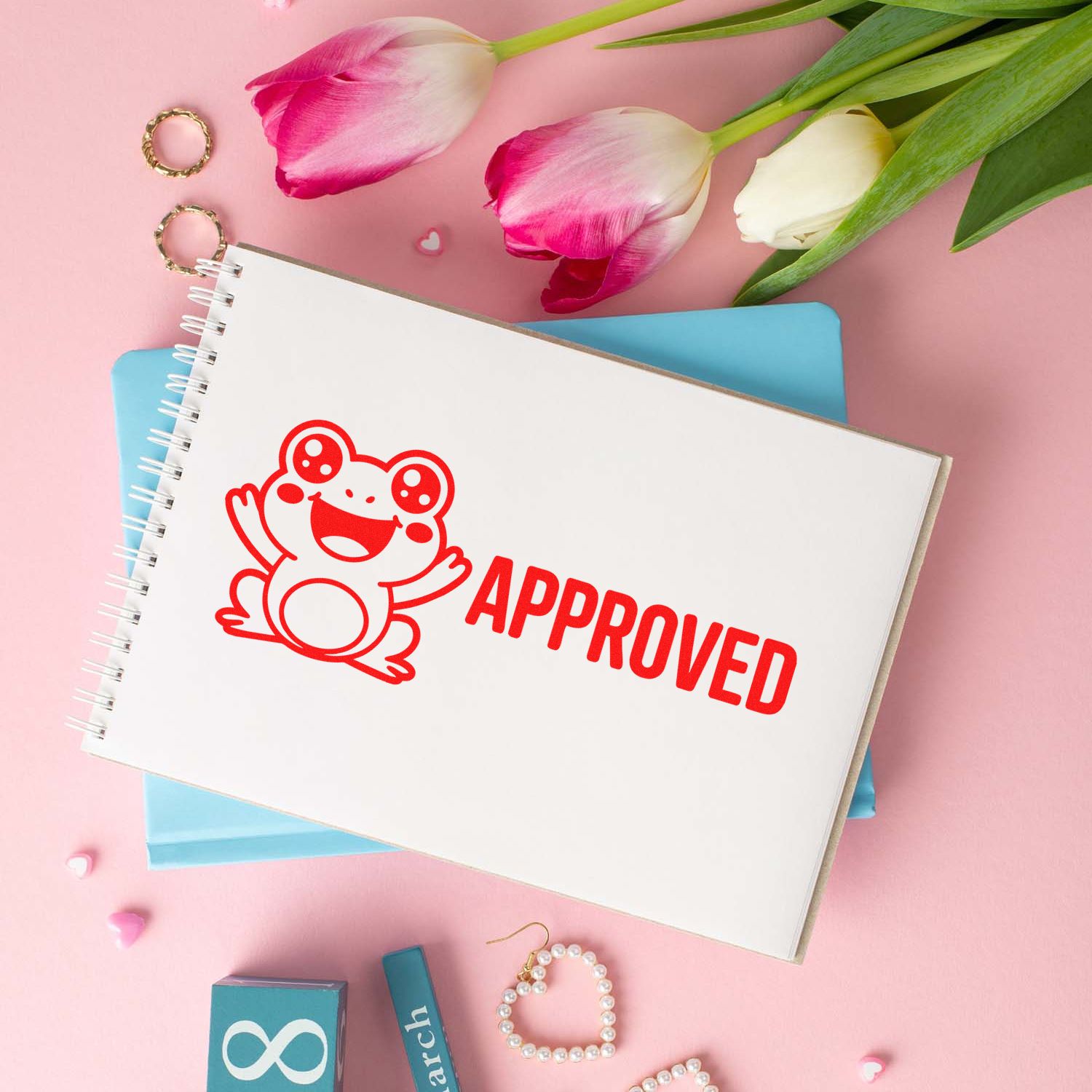 Cute frog approved rubber stamp on notebook, styled in a pink stationery flat lay with tulips.