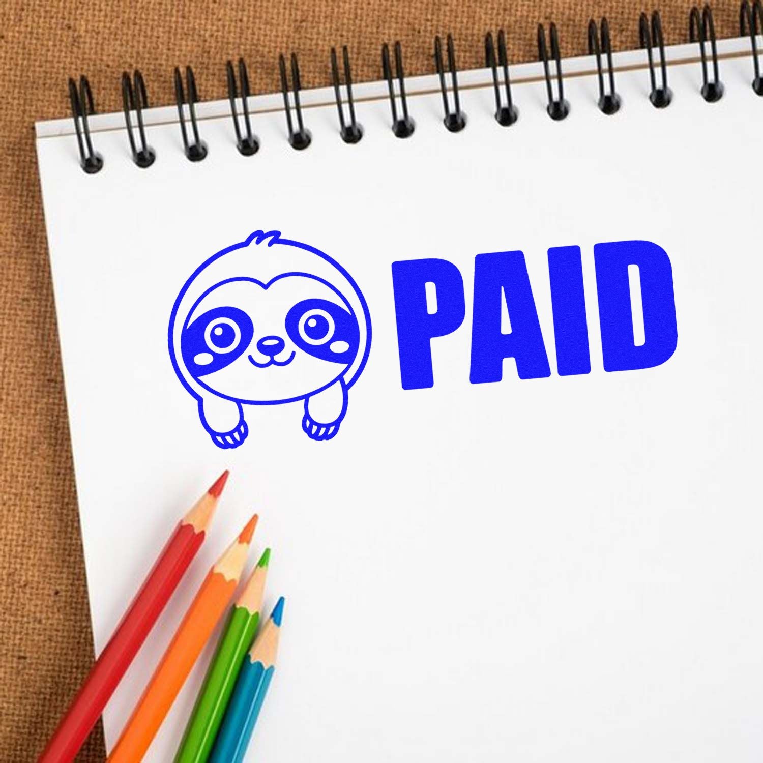 Blue PAID rubber stamp with cute sloth icon on a notebook, ideal for office accounting and payment status marking.