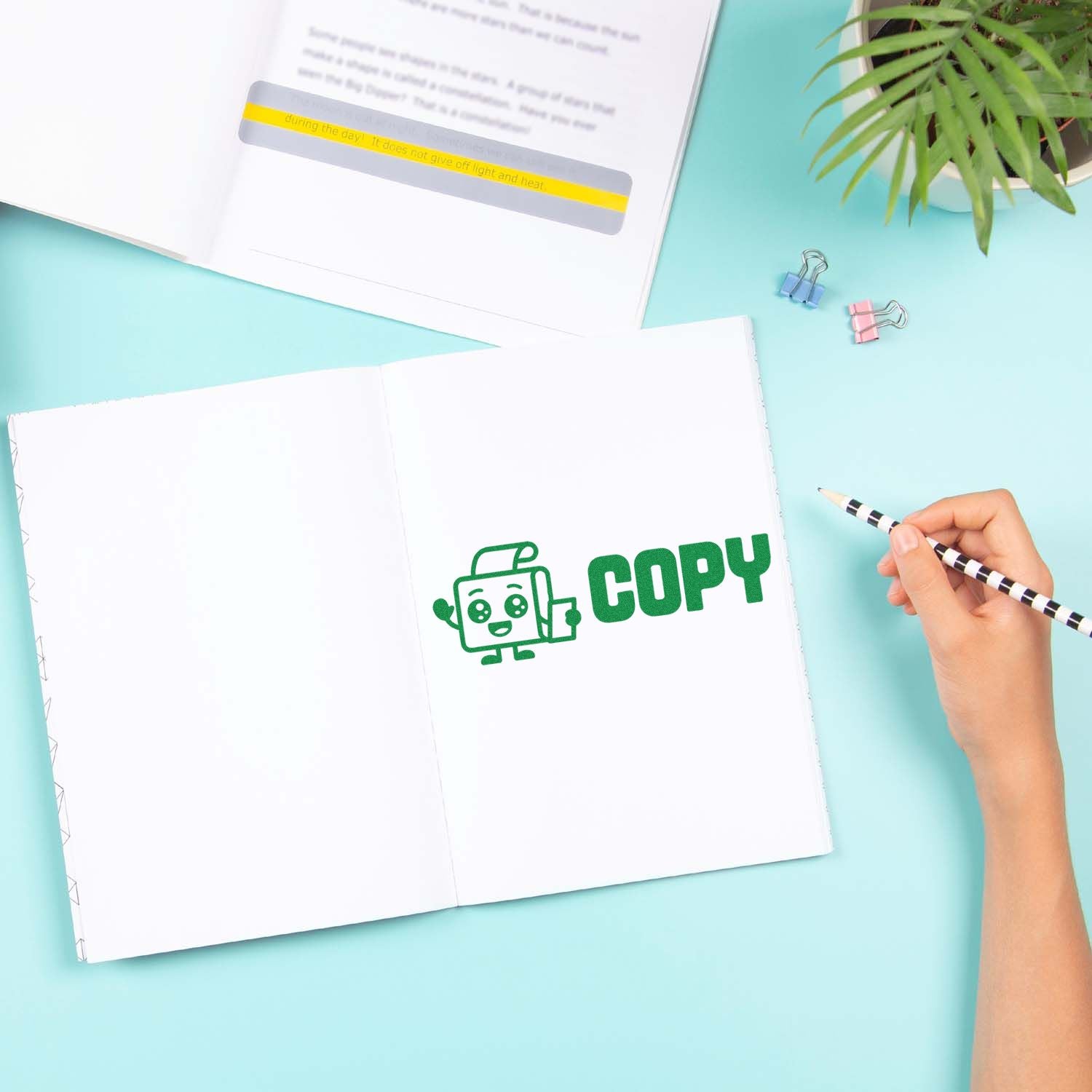 Copy rubber stamp impression in an open notebook, with hand holding pencil and stationery on a pastel workspace.