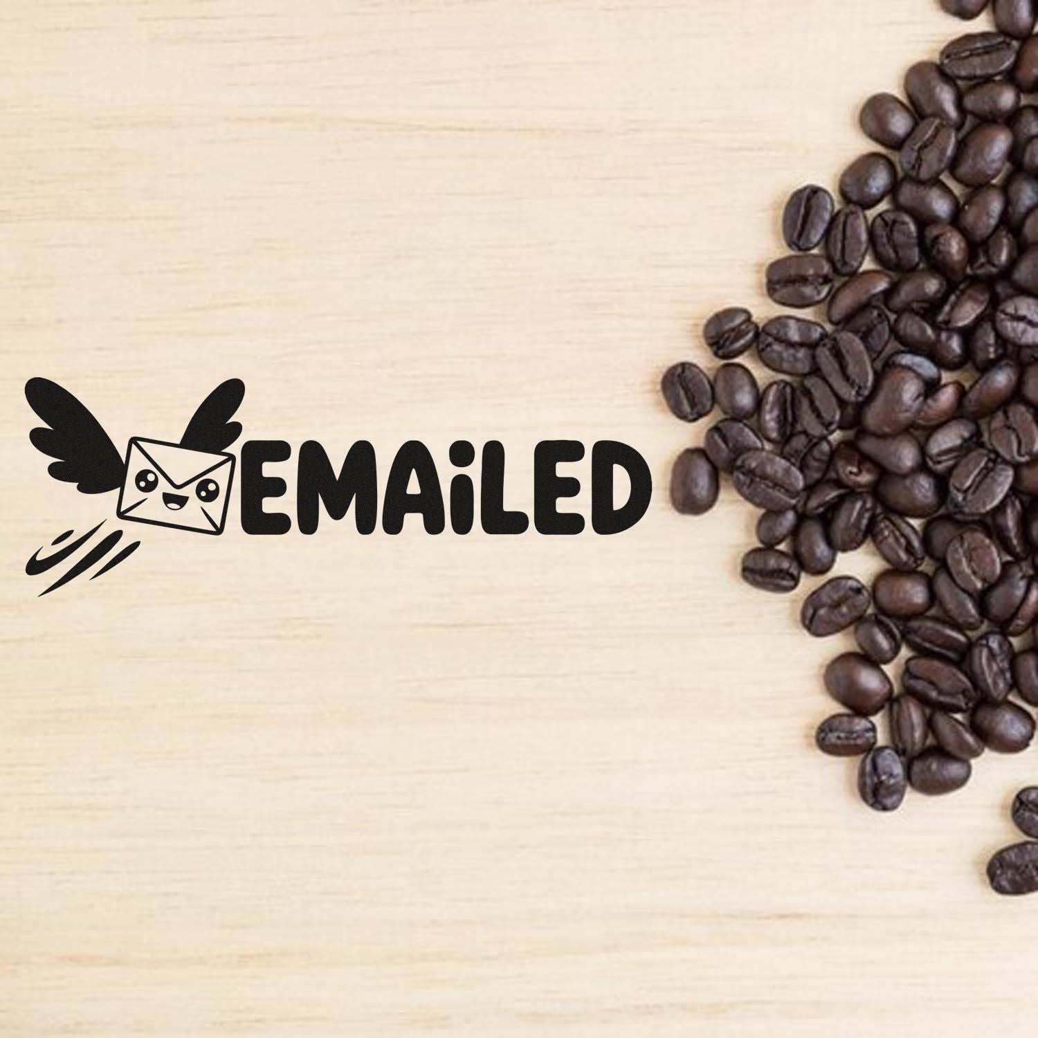Emailed rubber stamp with winged envelope icon for mail processing, shown on a wood background beside coffee beans.