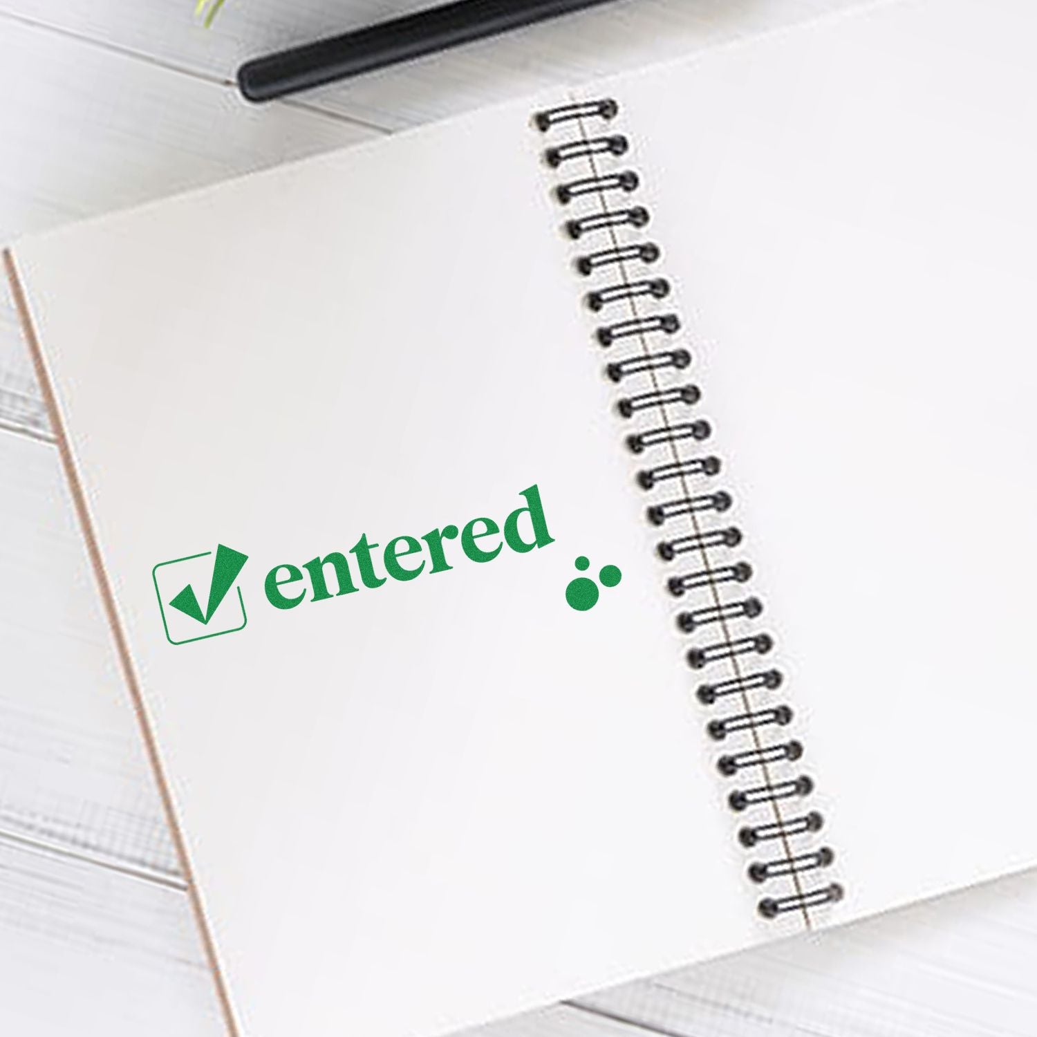 Green entered rubber stamp with checkmark on spiral notebook, ideal for office approval and recordkeeping