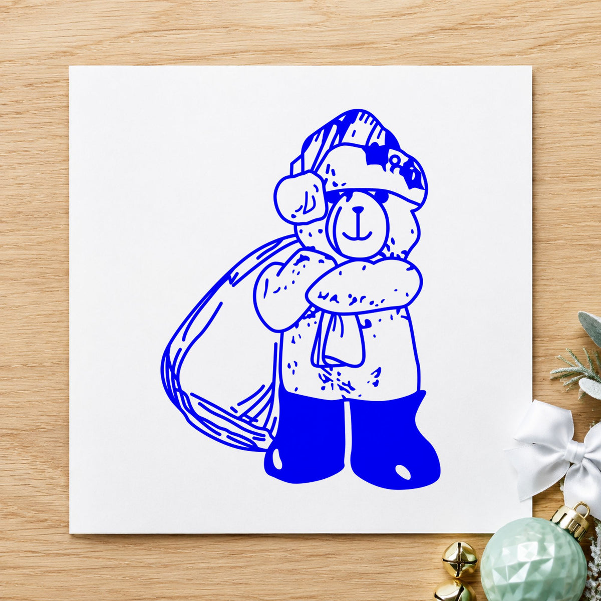 Blue festive card making stamp impression featuring the santa bear with gift bag design on white paper.