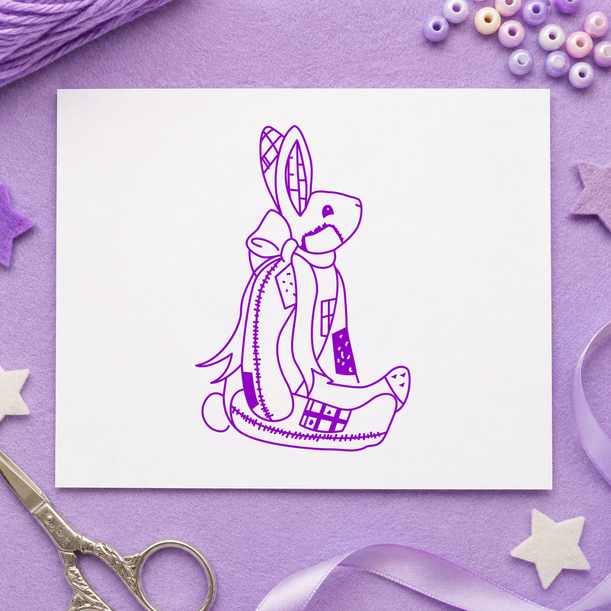 Patchwork Bunny with Bow Rubber Stamp impression in purple ink on white paper in a styled craft setting.