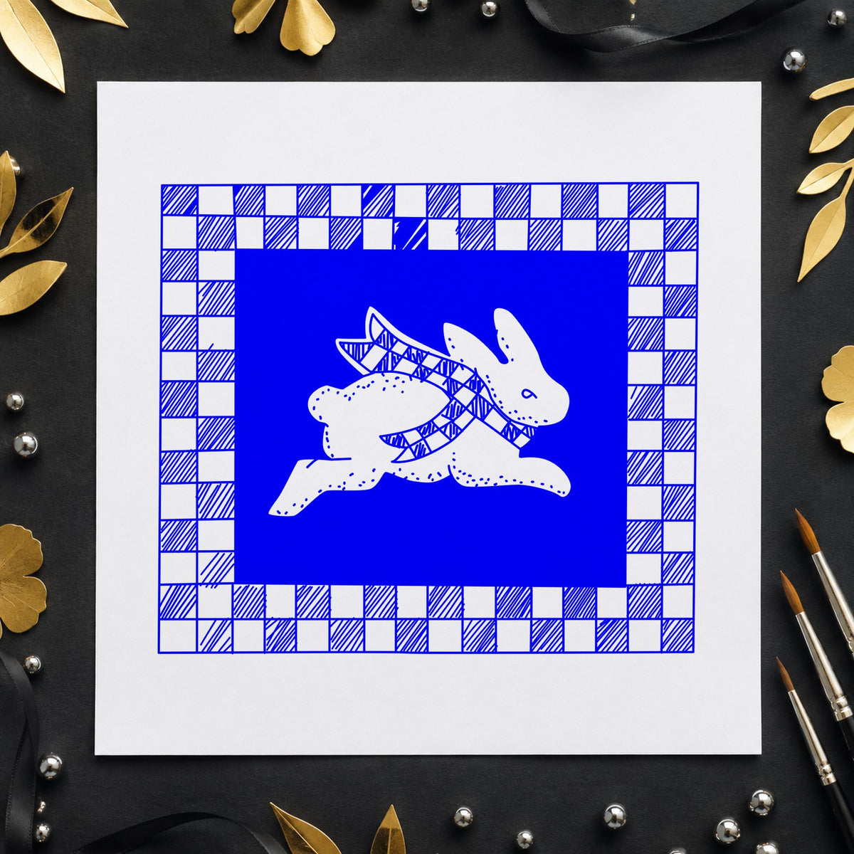 Rabbit with Checkered Border Rubber Stamp impression in blue ink on white paper in a styled craft setting.
