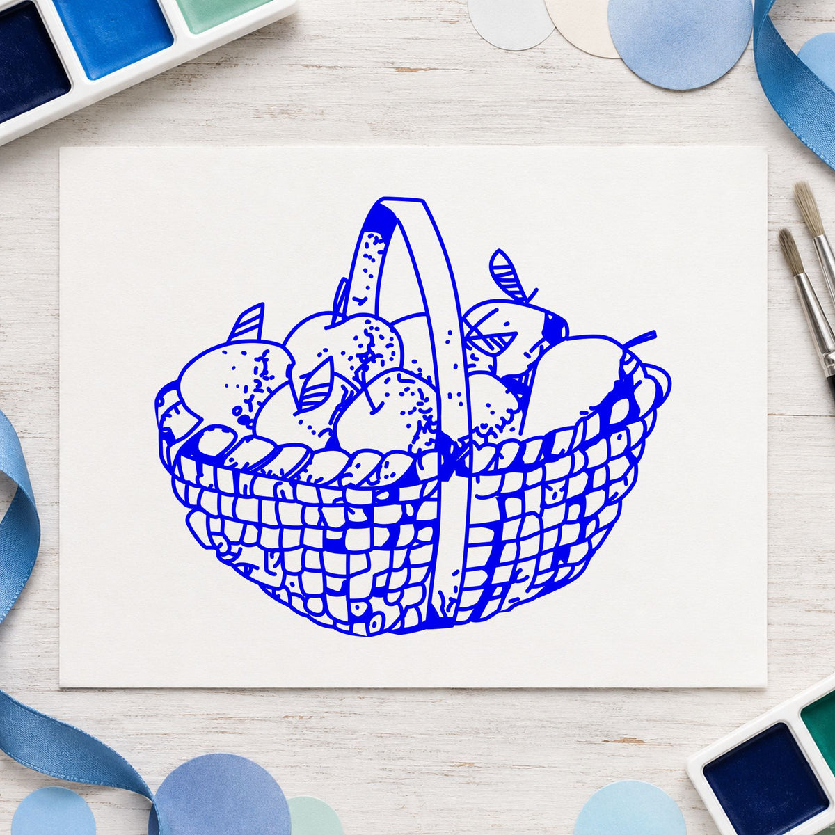 Round Apple Basket Rubber Stamp impression in blue ink on white paper in a styled craft setting.