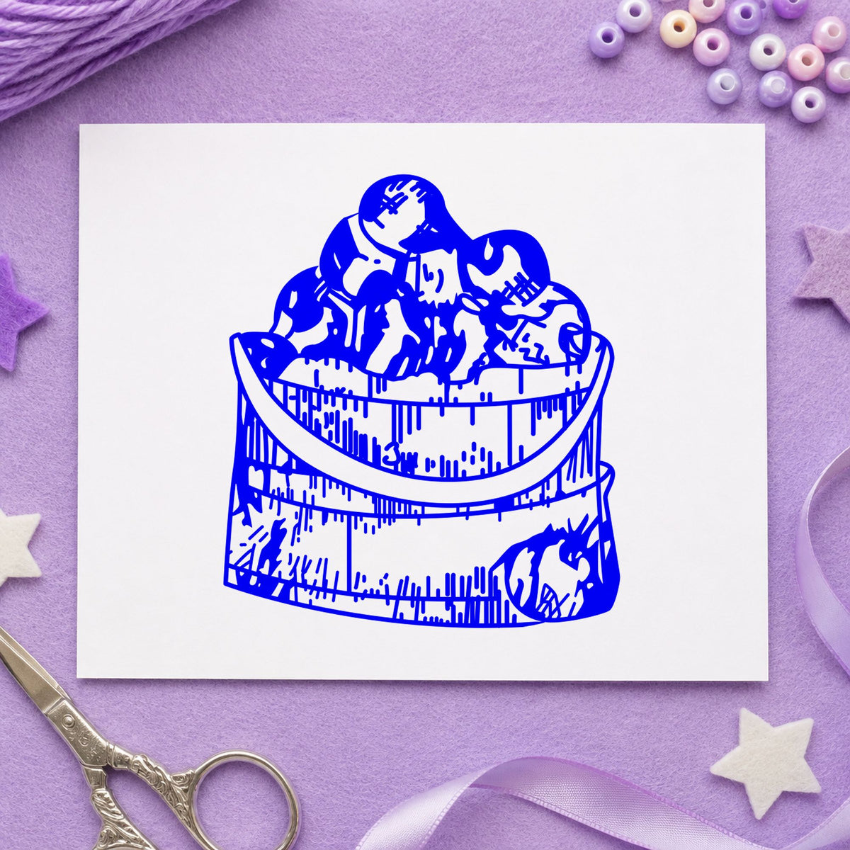 Wooden Bucket of Apples Rubber Stamp impression in blue ink on white paper in a styled craft setting.