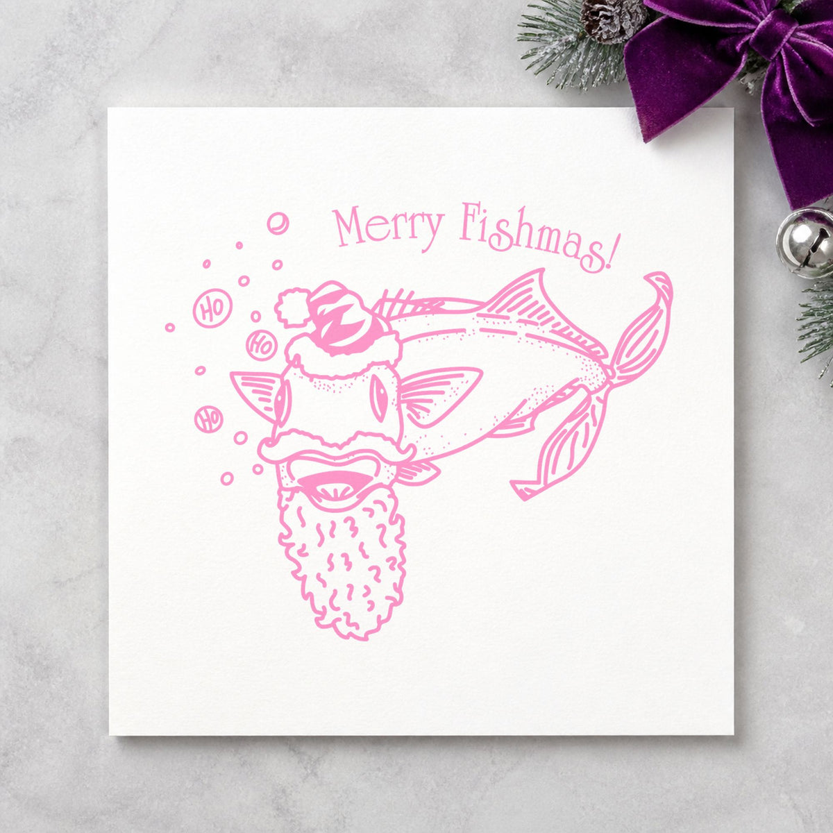 Merry Fishmas Catfish Rubber Stamp impression in pink ink on white paper in a styled craft setting.