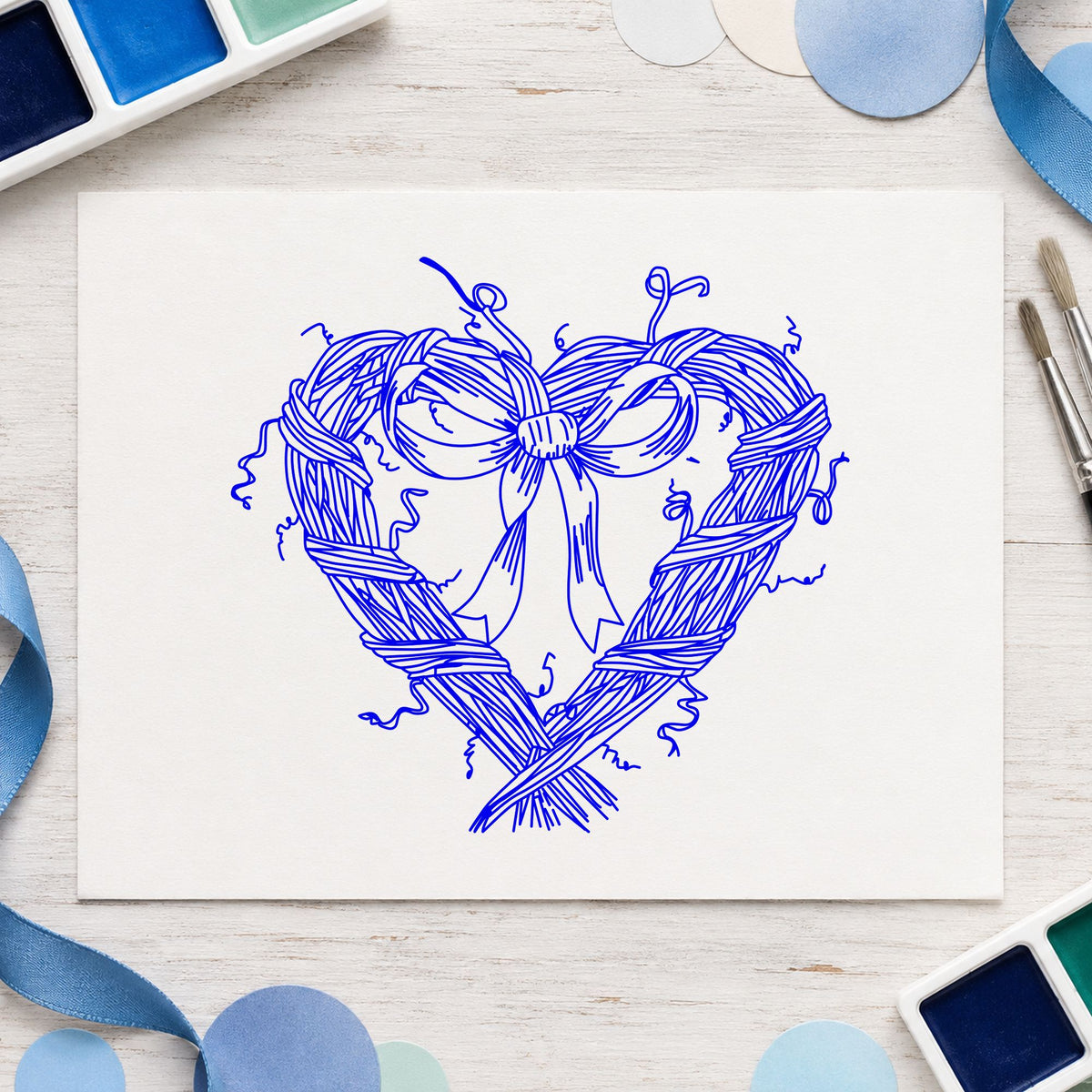 Heart Wreath with Bow Rubber Stamp impression in blue ink on white paper in a styled craft setting.