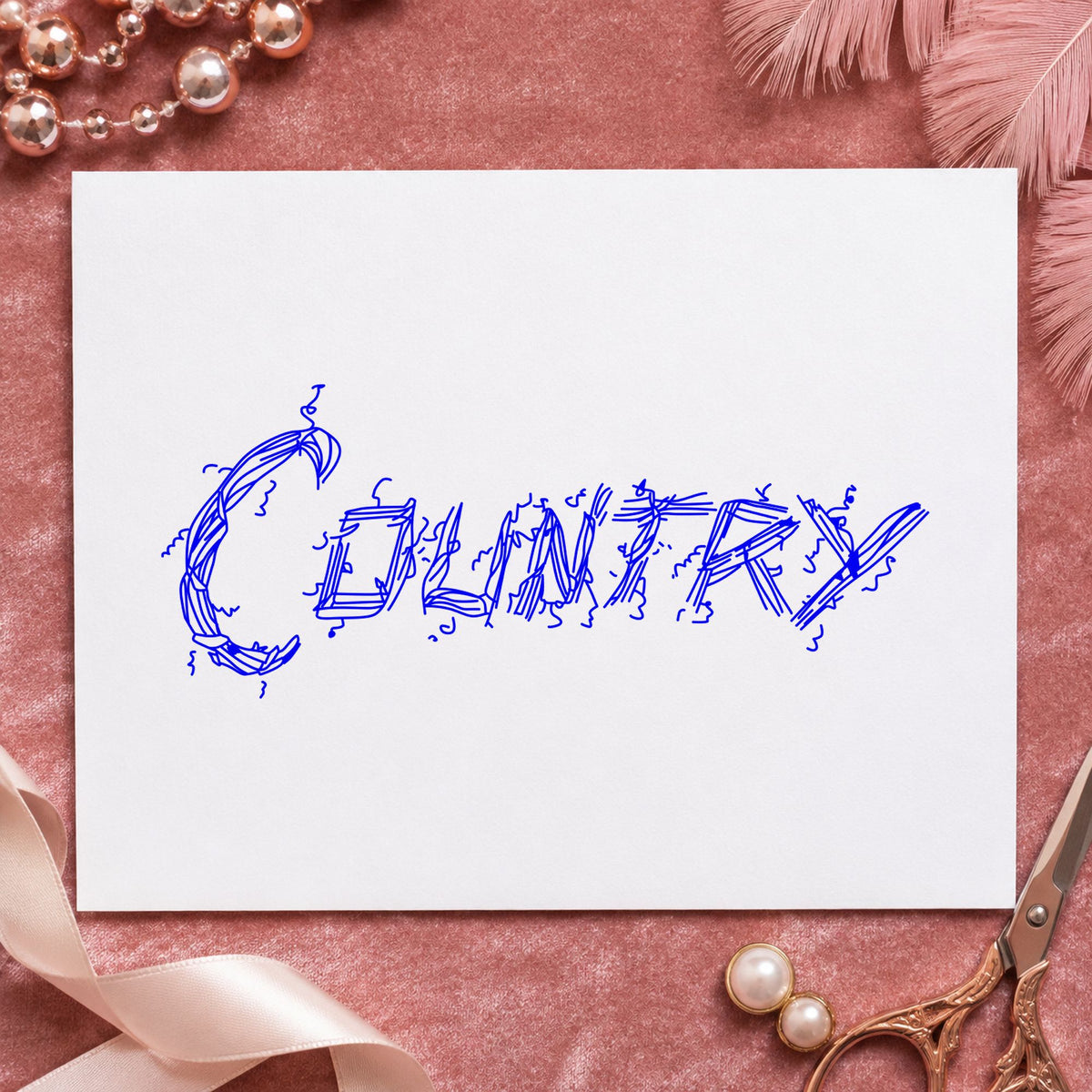 Country Lettering Rubber Stamp impression in blue ink on white paper in a styled craft setting.
