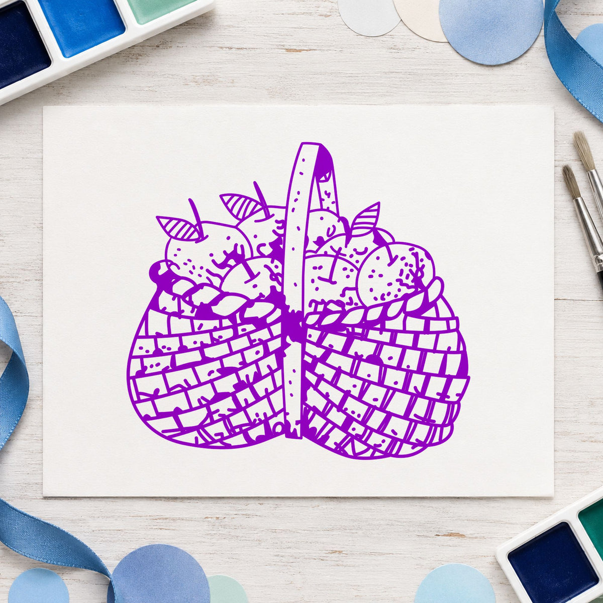 Basket Brimming with Apples Rubber Stamp impression in purple ink on white paper in a styled craft setting.