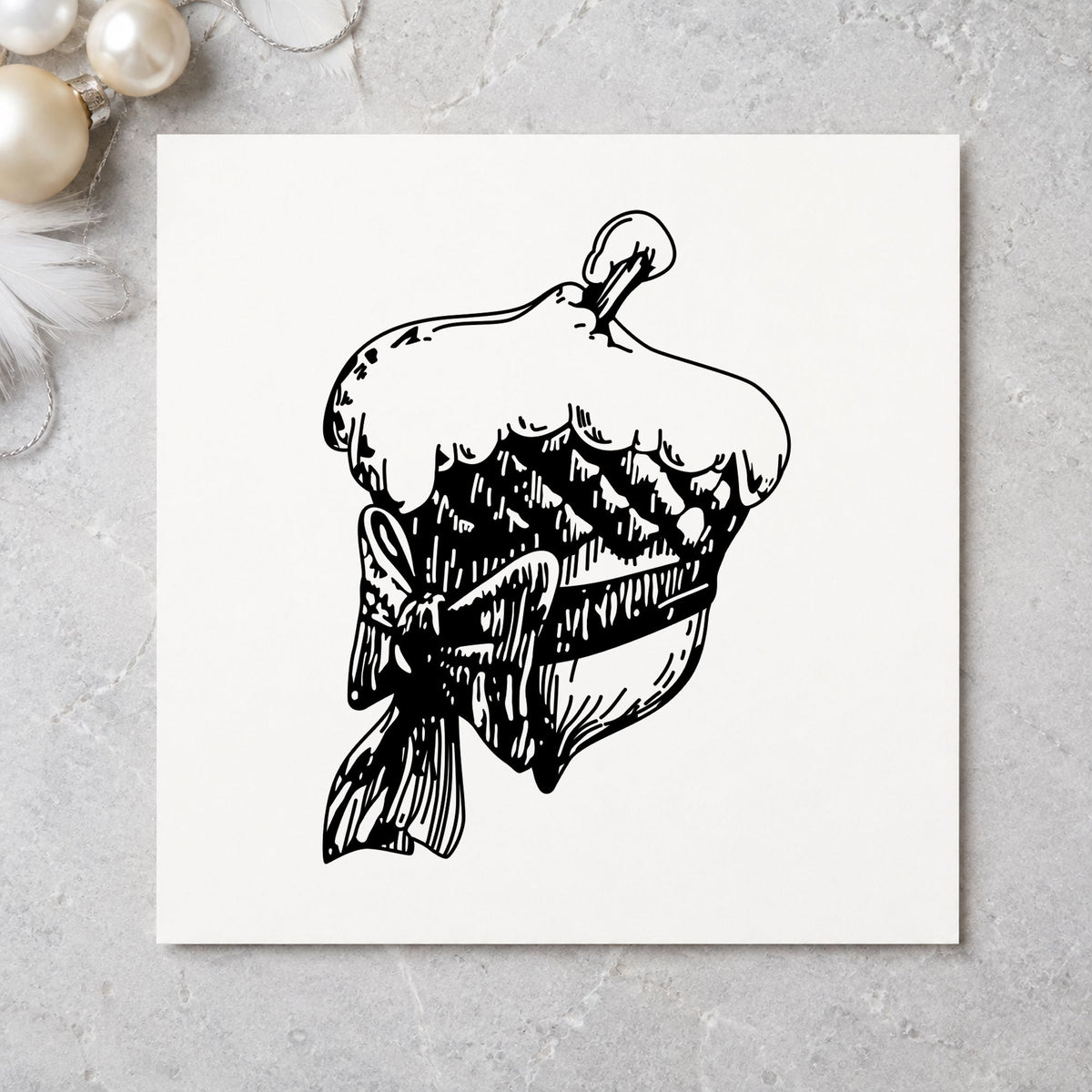 Snowy Acorn with Bow Christmas Rubber Stamp impression in black ink on white paper in a styled craft setting.