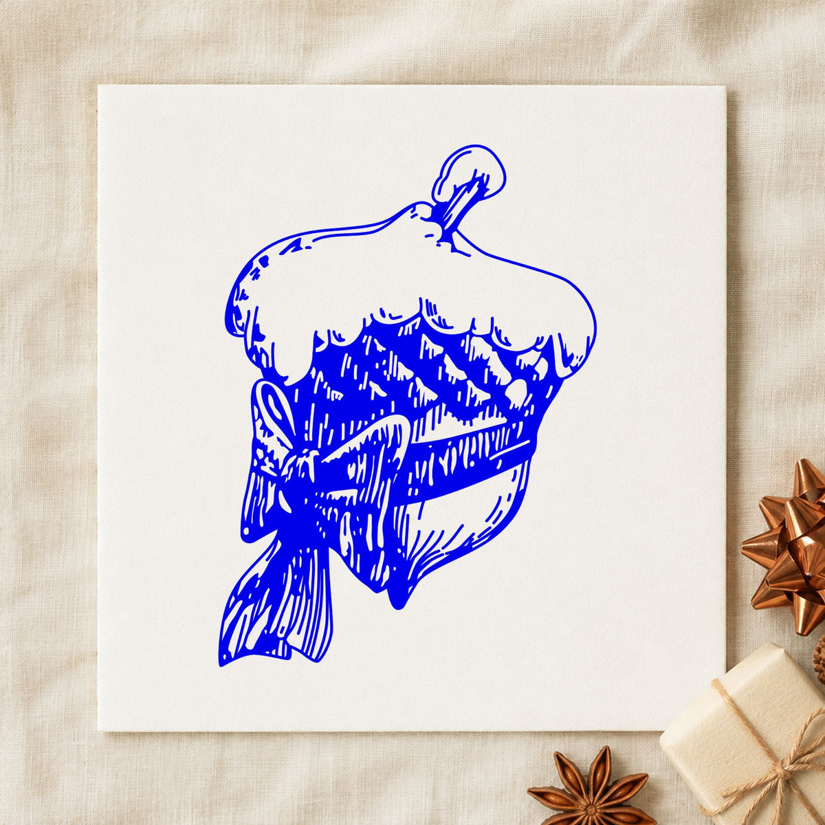 Snowy Acorn with Bow Christmas Rubber Stamp impression in blue ink on white paper in a styled craft setting.