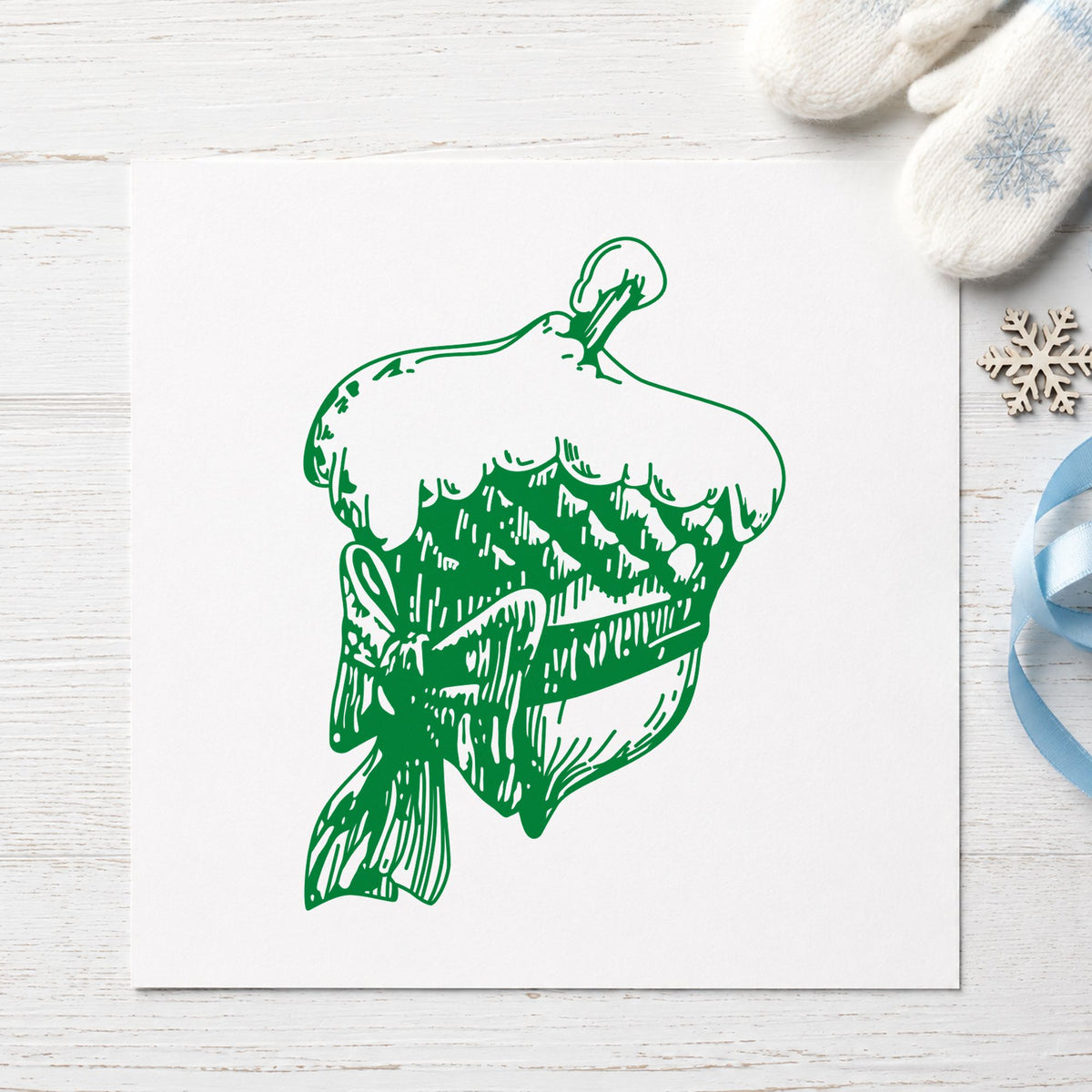 Snowy Acorn with Bow Christmas Rubber Stamp impression in green ink on white paper in a styled craft setting.