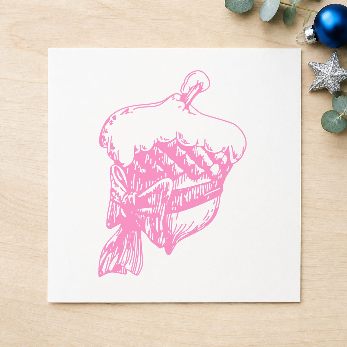 Snowy Acorn with Bow Christmas Rubber Stamp impression in pink ink on white paper in a styled craft setting.