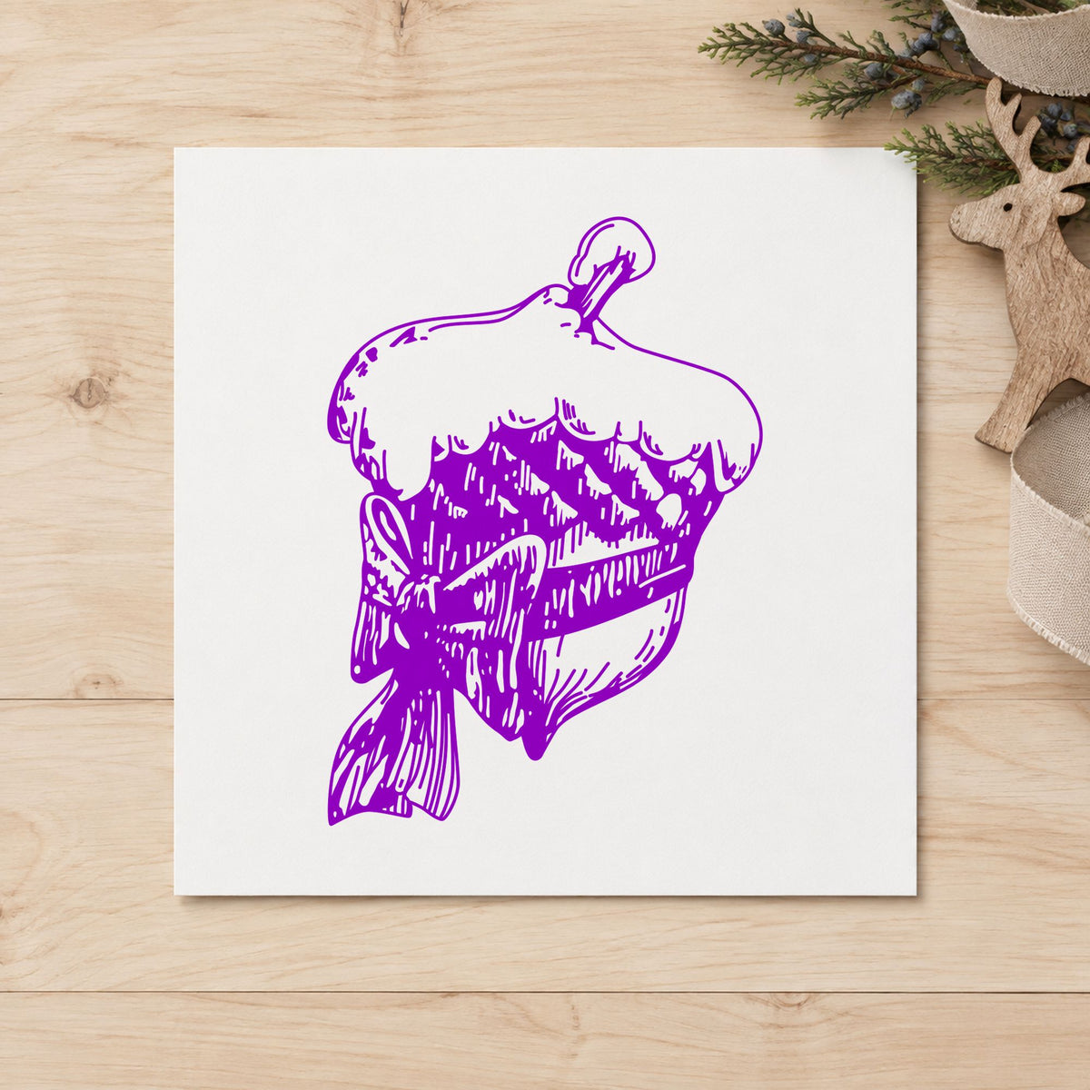 Snowy Acorn with Bow Christmas Rubber Stamp impression in purple ink on white paper in a styled craft setting.