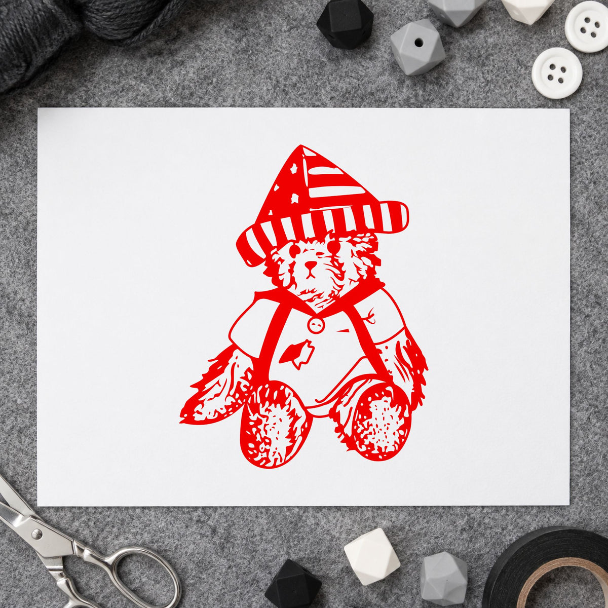 Bear in Stars and Stripes Hat Rubber Stamp impression in red ink on white paper in a styled craft setting.