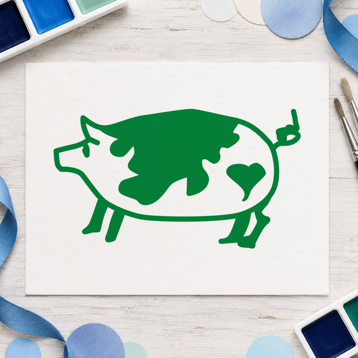 Spotted Pig with Heart Rubber Stamp impression in green ink on white paper in a styled craft setting.