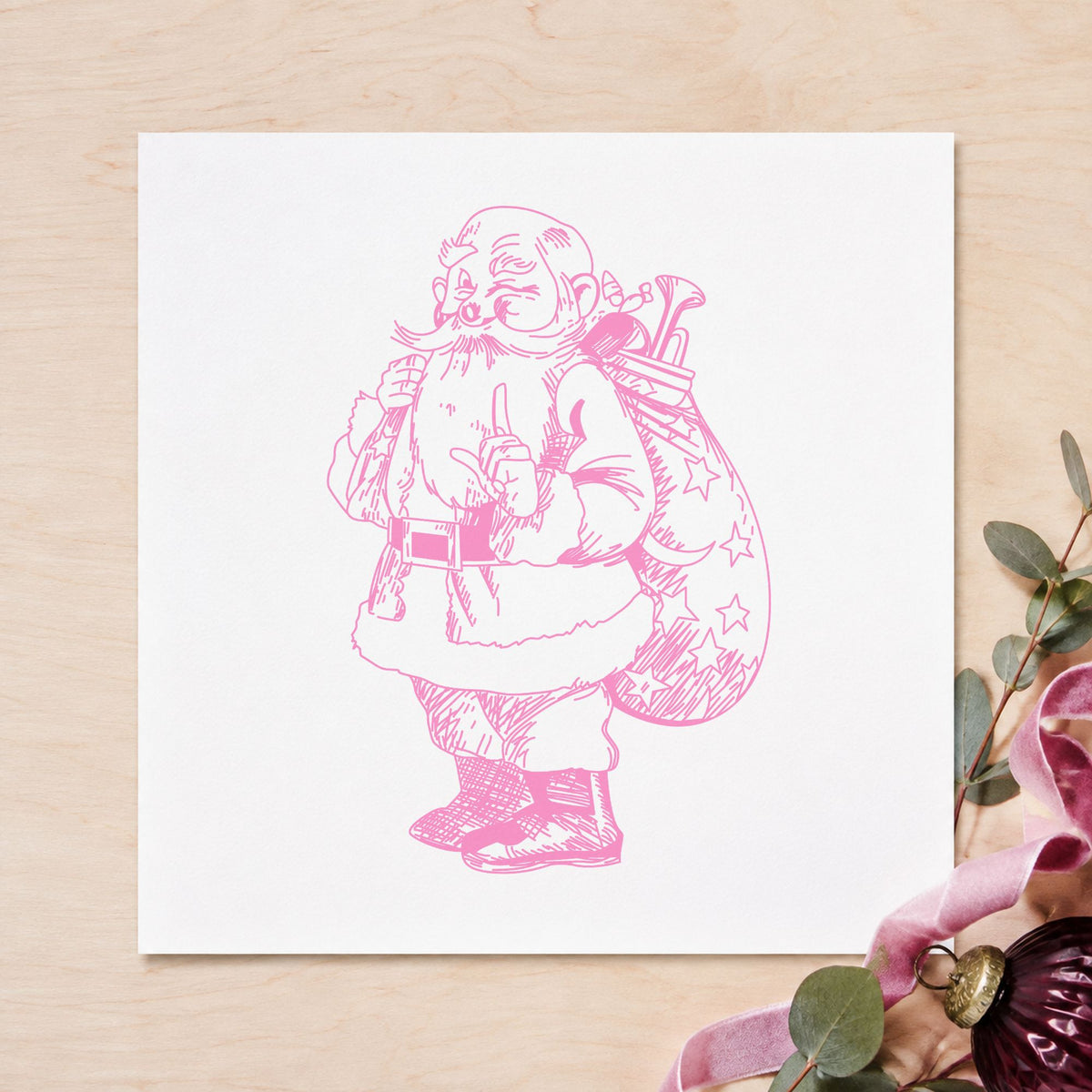 Santa with Gift Sack Rubber Stamp impression in pink ink on white paper in a styled craft setting.