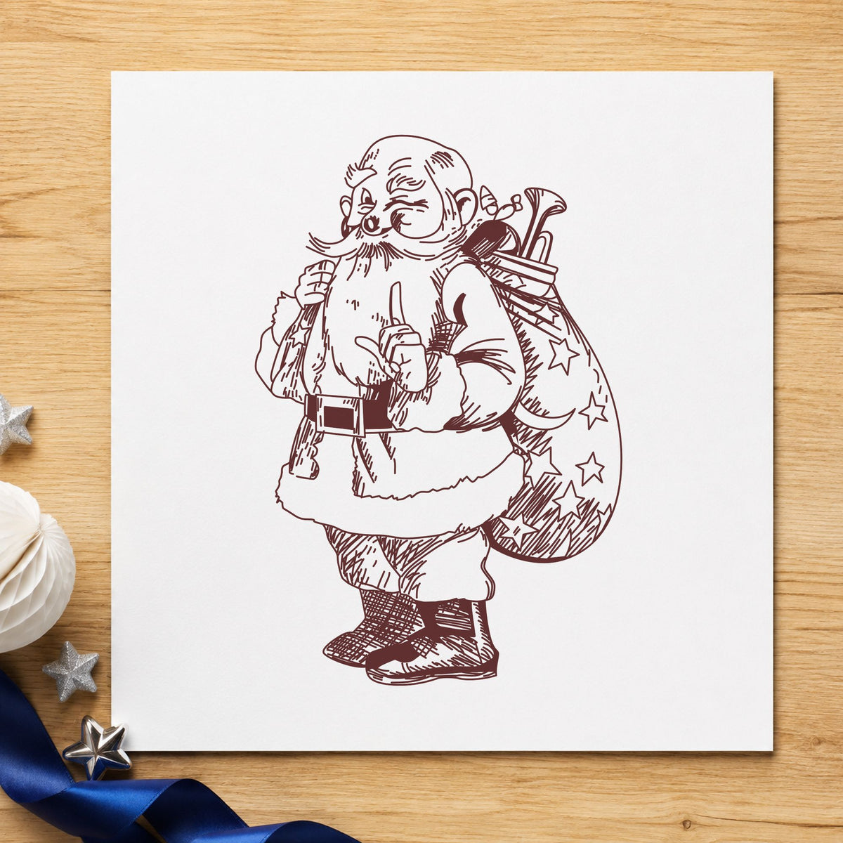 Santa with Gift Sack Rubber Stamp impression in brown ink on white paper in a styled craft setting.